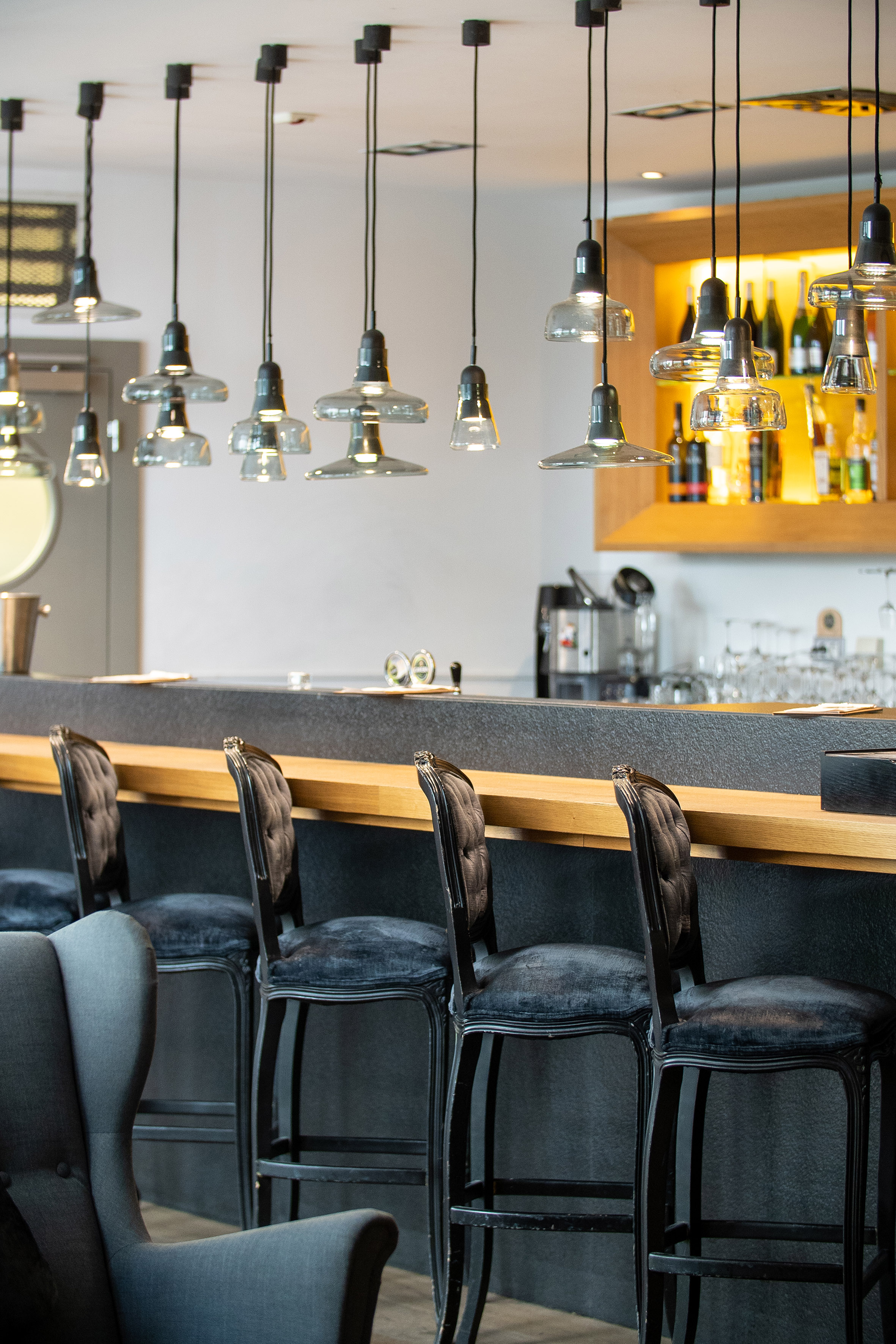 Modern bar, pendant lights, black velvet bar stools, and wooden counter.