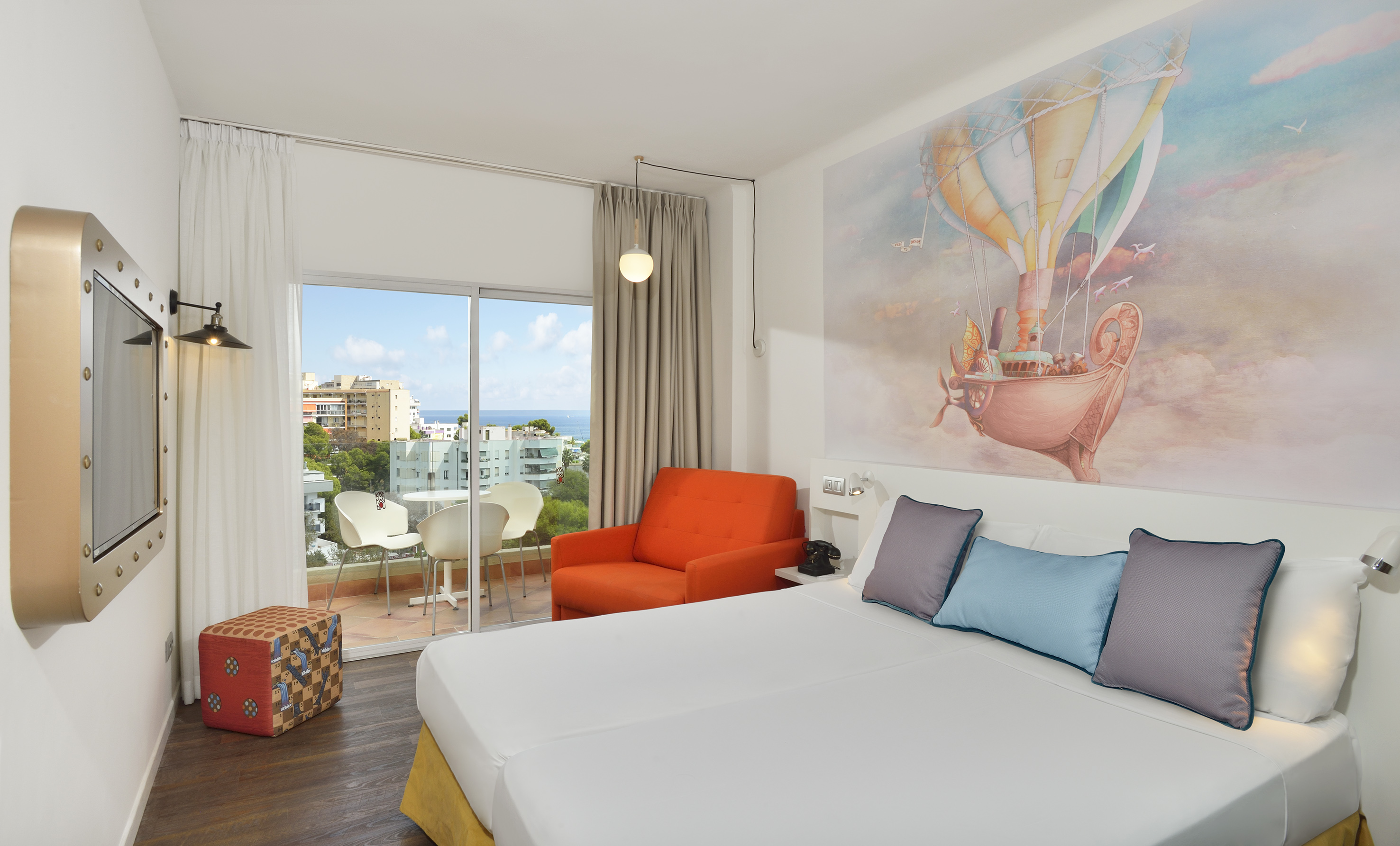 Bright hotel room with hot air balloon mural and sea view balcony.