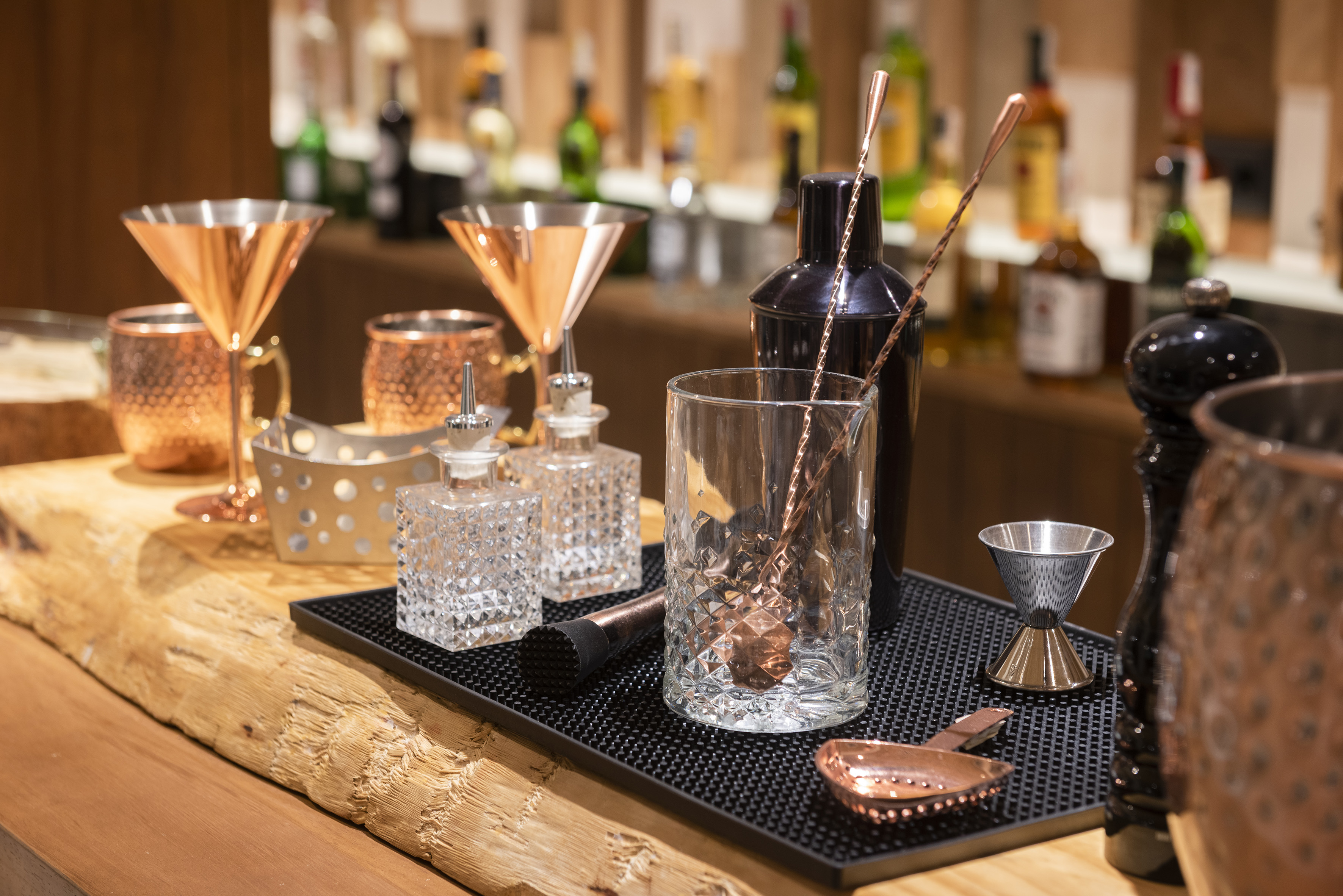 Copper martini glasses, shaker, and bar tools on a rustic wooden bar.