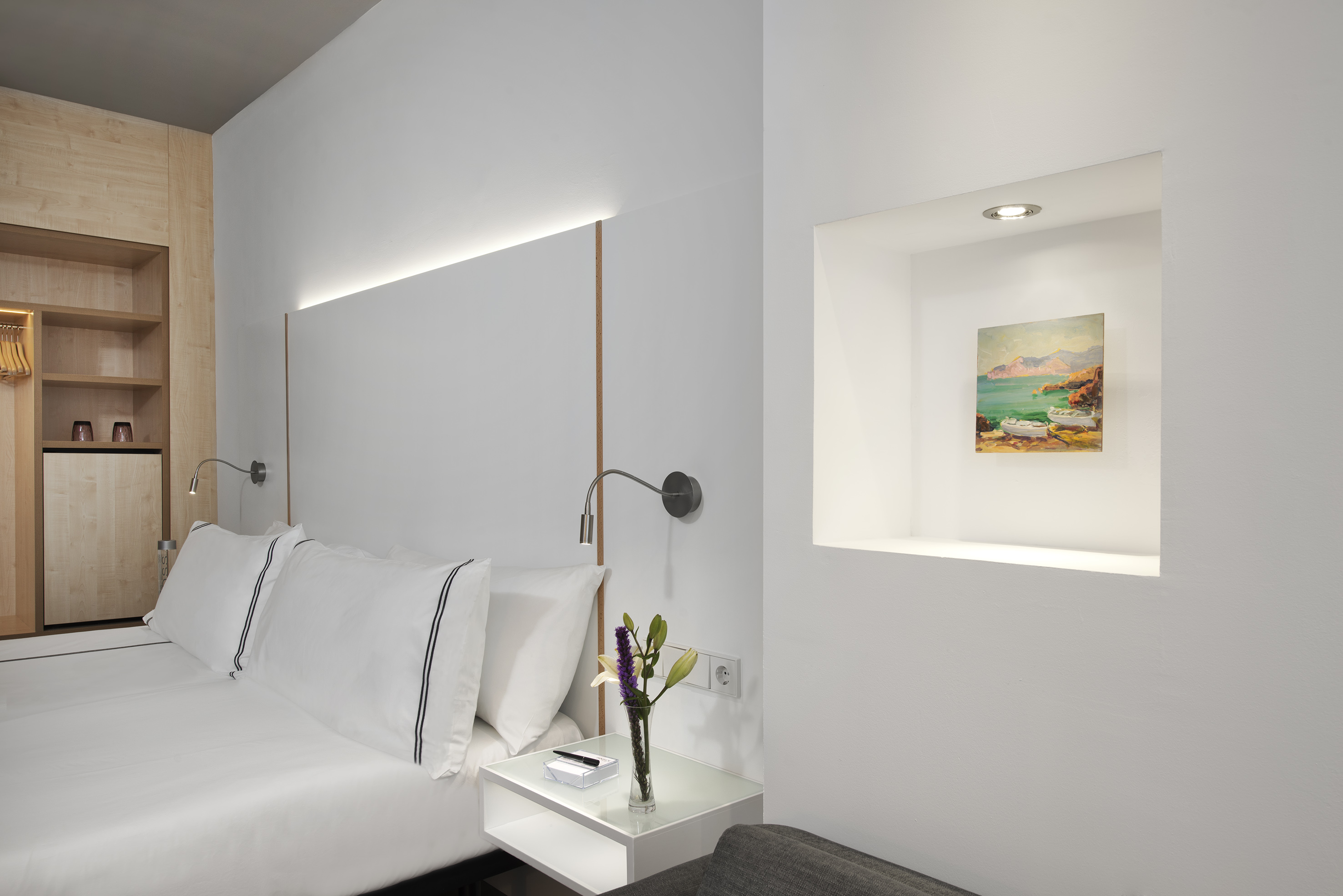 Modern hotel room with white bed, wooden wardrobe, and illuminated wall art.