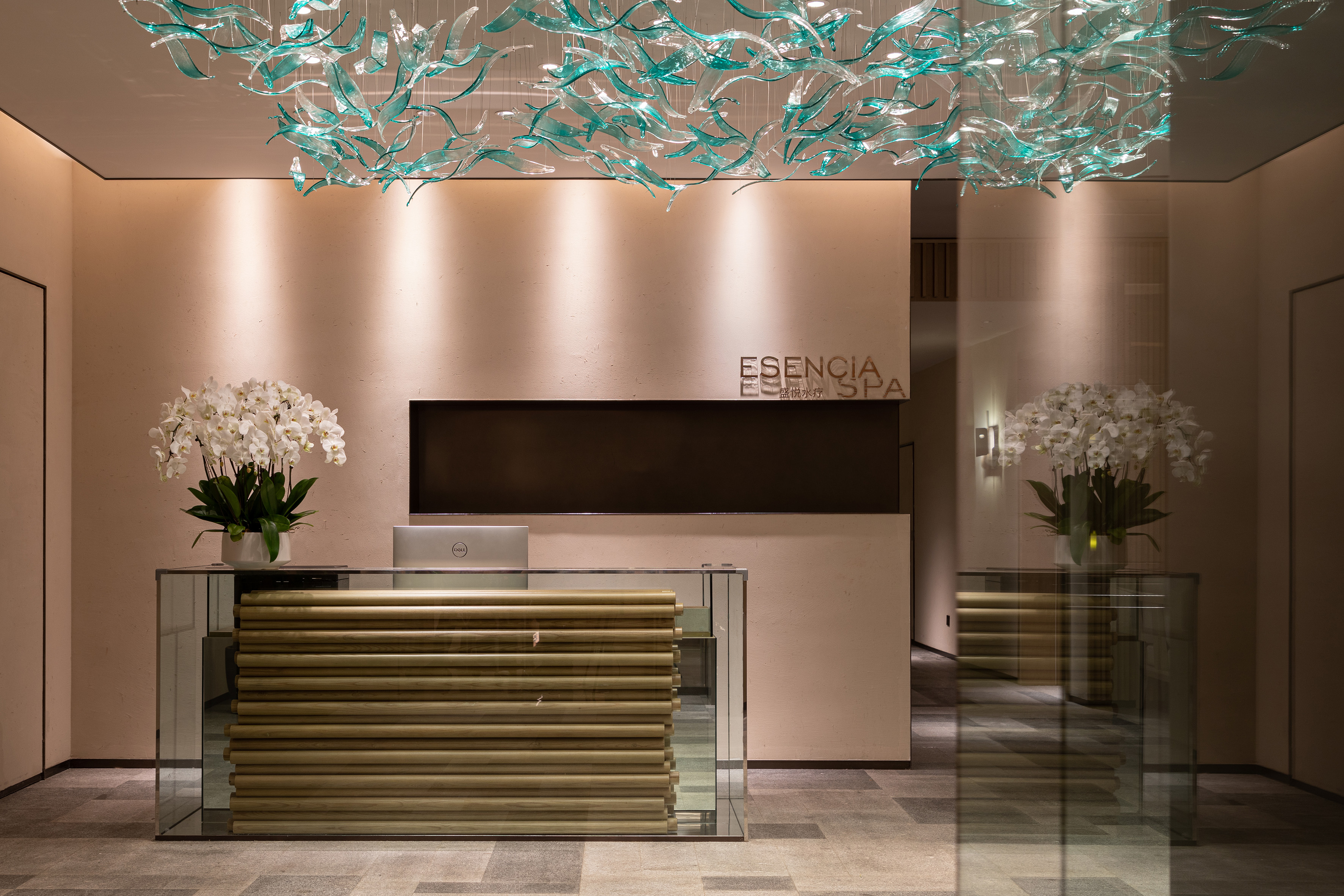 Esencia Spa reception with wave chandelier, wooden desk, and orchids.