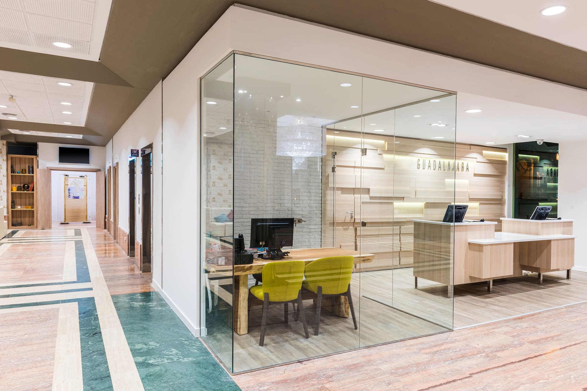 Modern office interior: glass meeting room, wood desk, green chairs, reception.