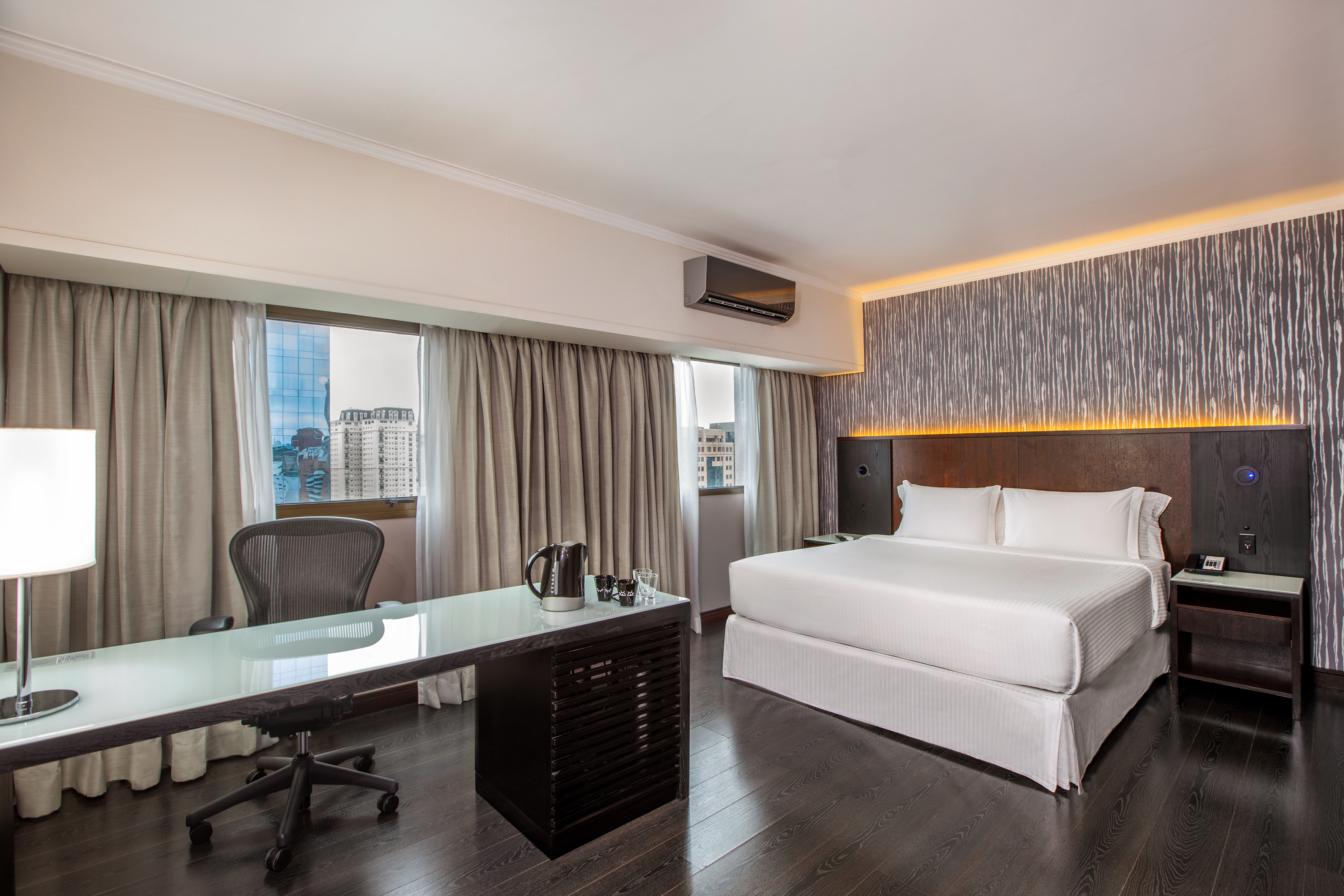 Modern hotel room with king bed, desk, and window city view.
