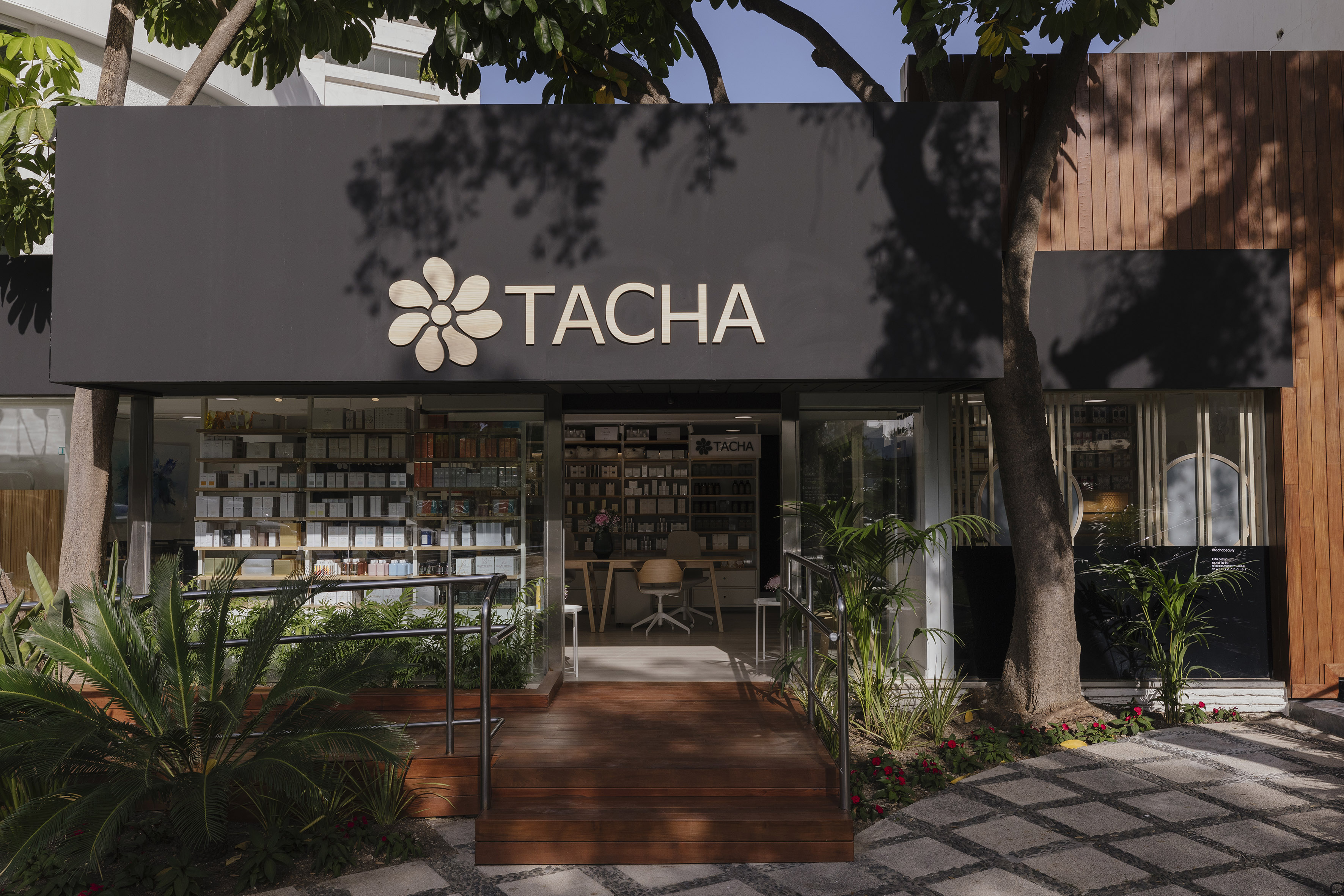 Tacha skincare store entrance with black facade, gold logo, and lush plants.