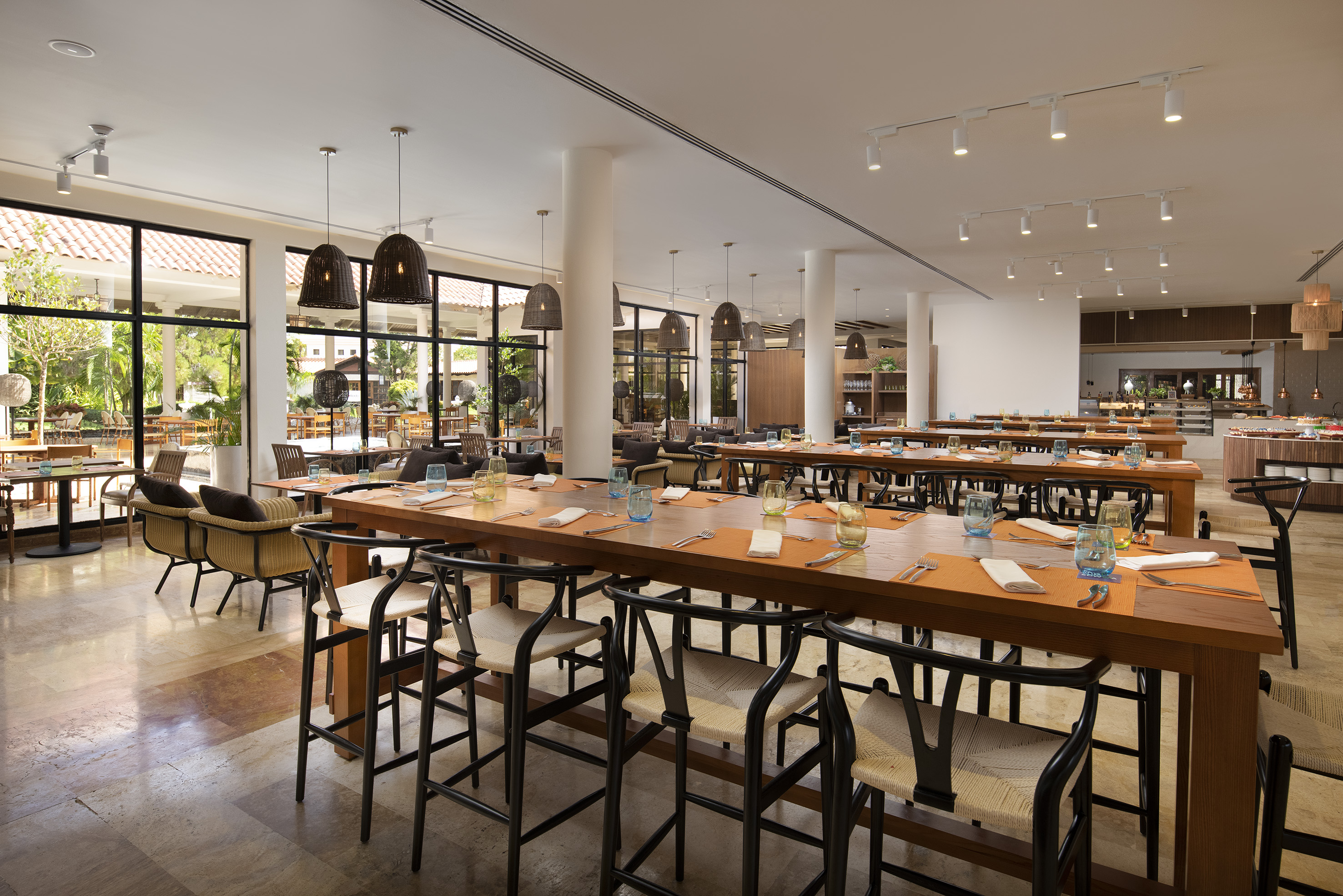Spacious resort restaurant with long dining tables, modern chairs, and garden views.