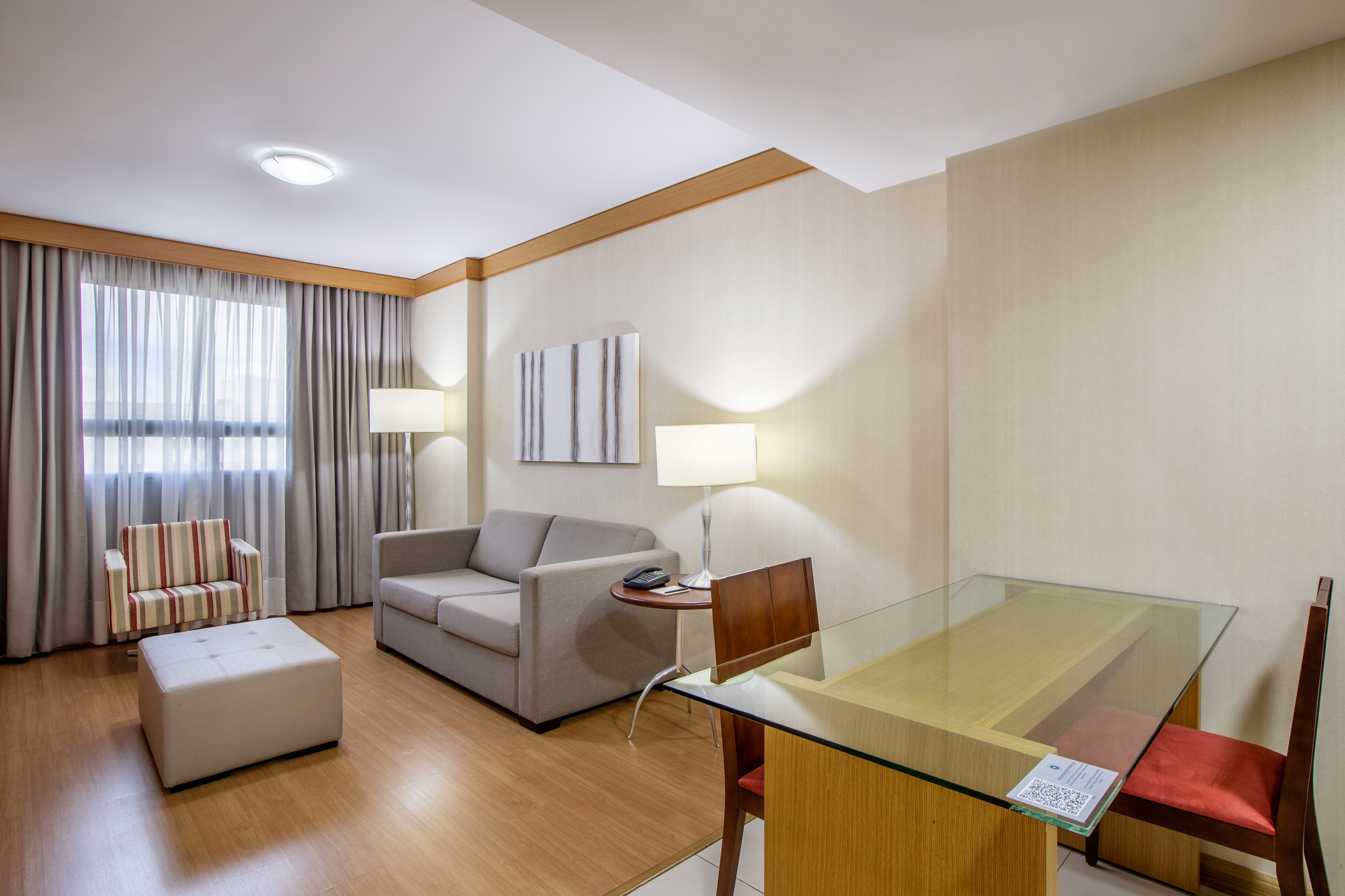 Hotel suite living room with gray sofa, striped armchair, glass desk, wood floor.