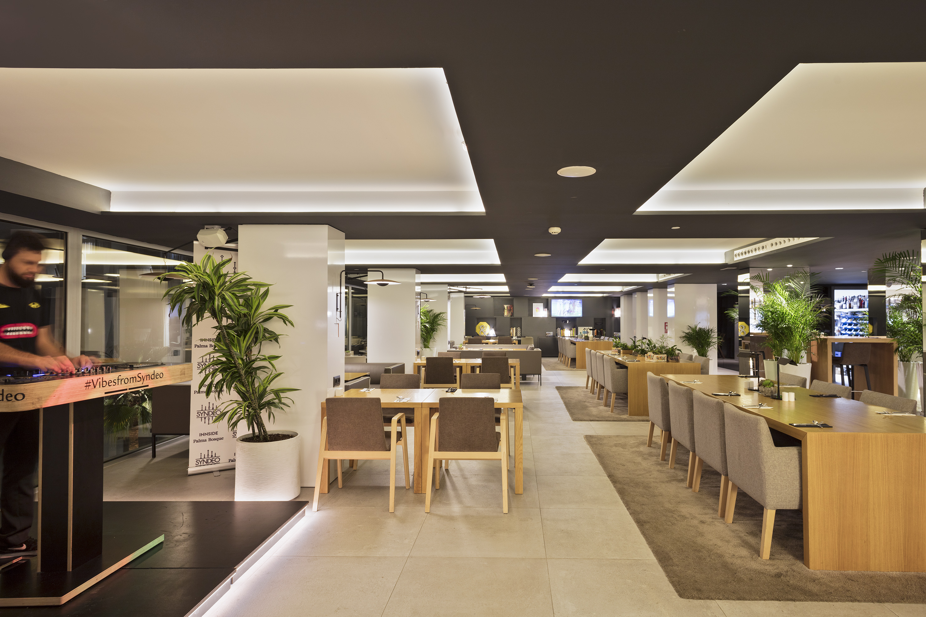 Modern hotel restaurant lounge with DJ booth, long dining tables, and sleek decor.
