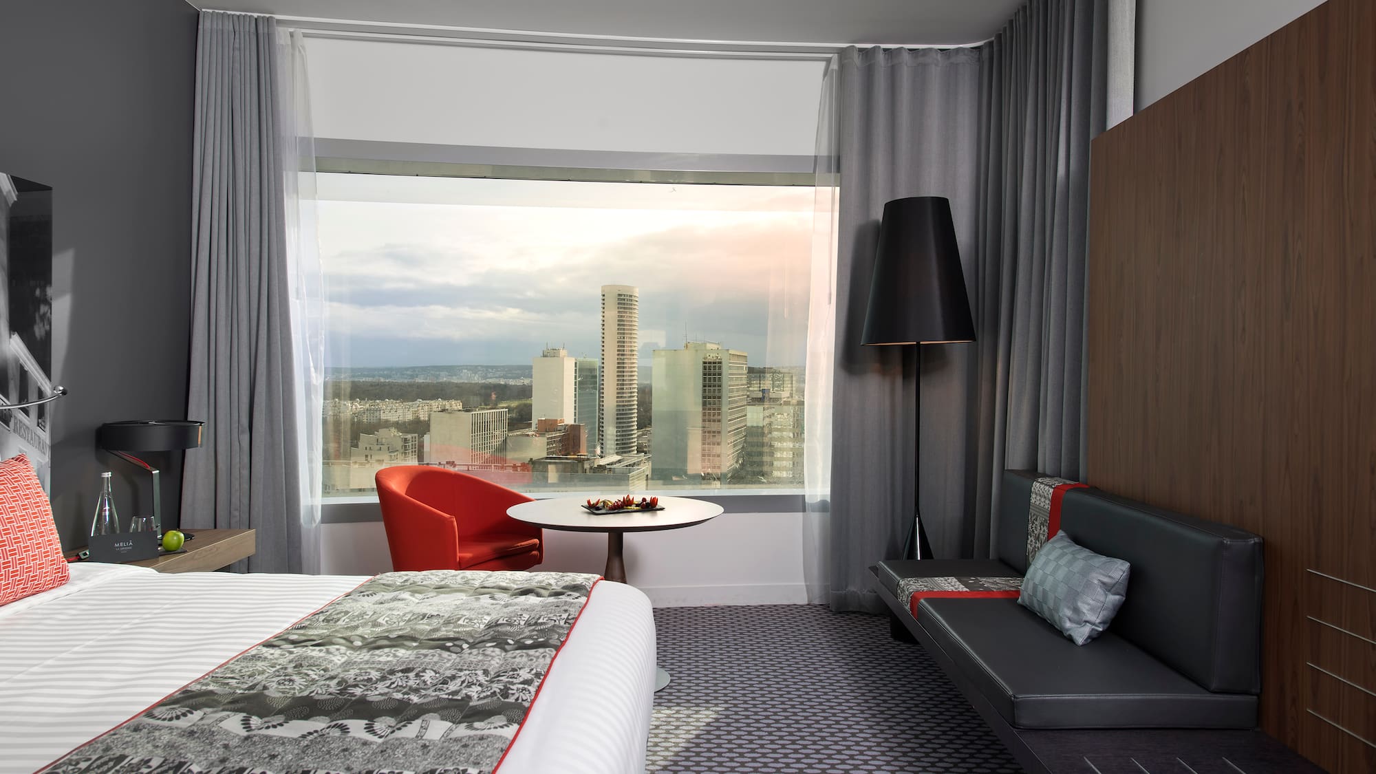a room with a bed and a table and a window with a city view