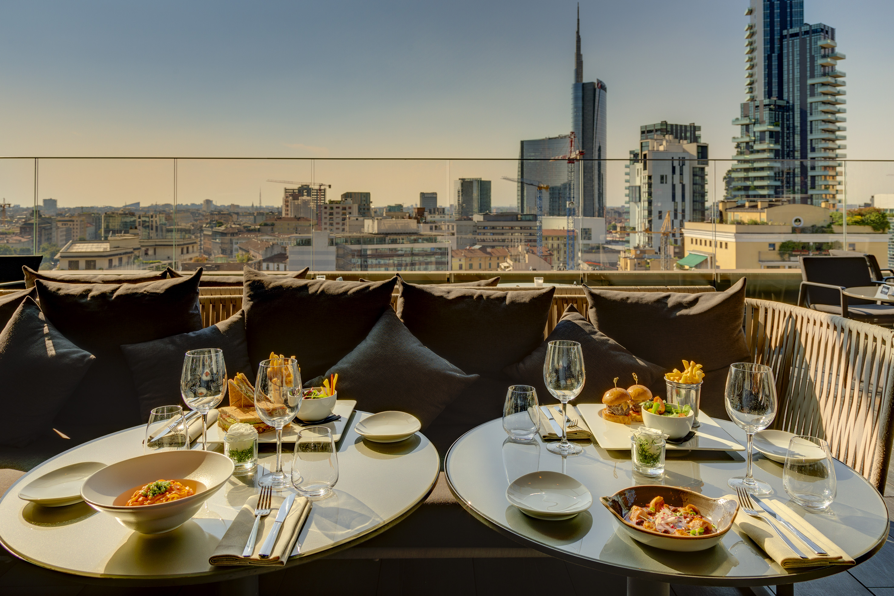 Sunny Milan rooftop restaurant with food, drinks, and panoramic city views.