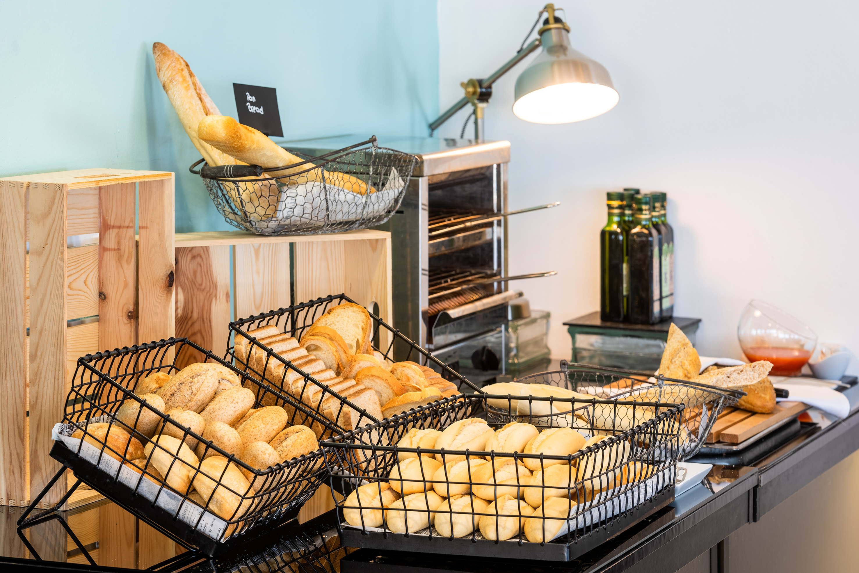 Fresh bread buffet featuring baguettes, rolls, and sliced bread next to a toaster.