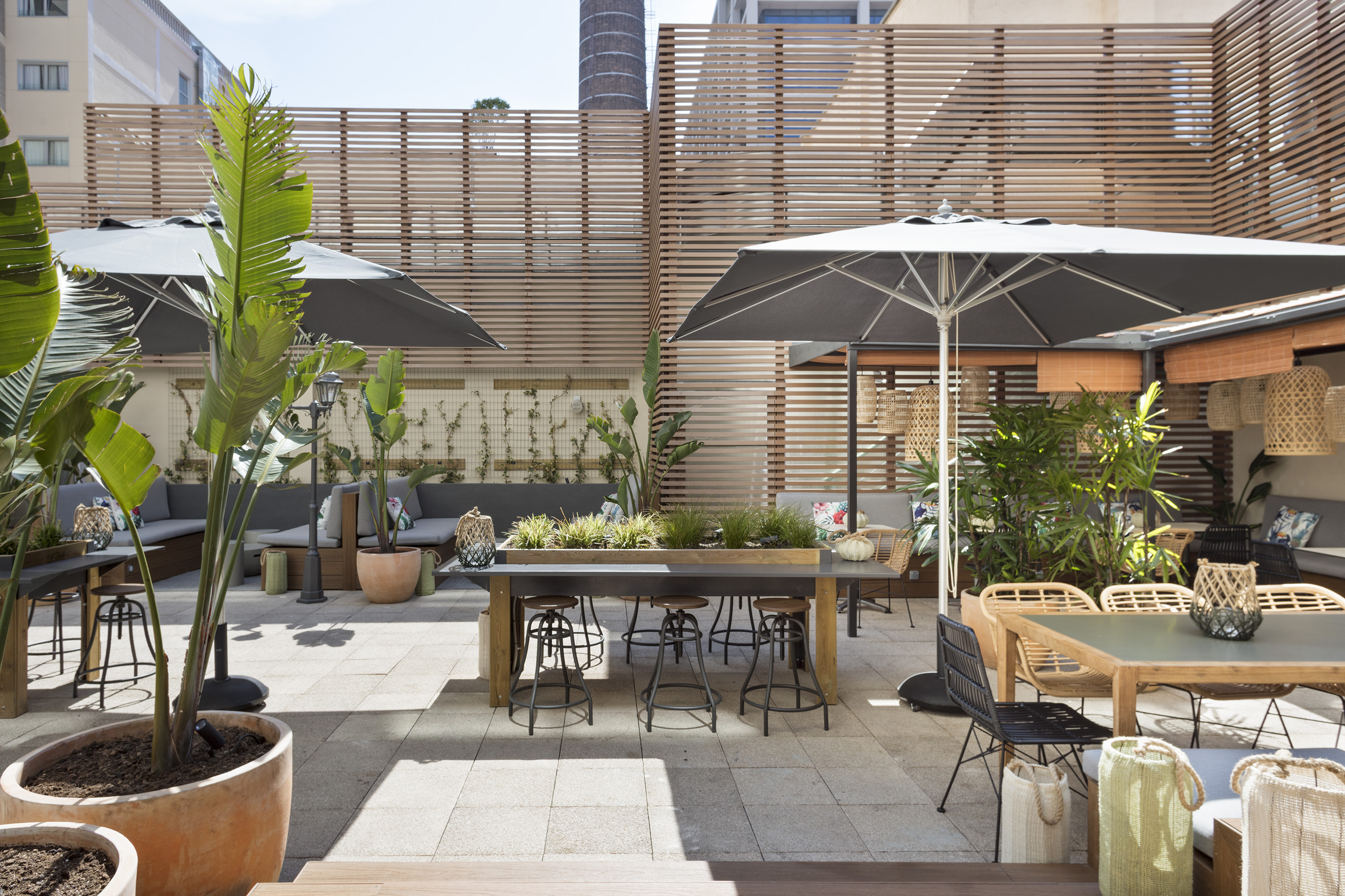 Modern outdoor patio lounge with diverse seating, sun umbrellas, and lush greenery.