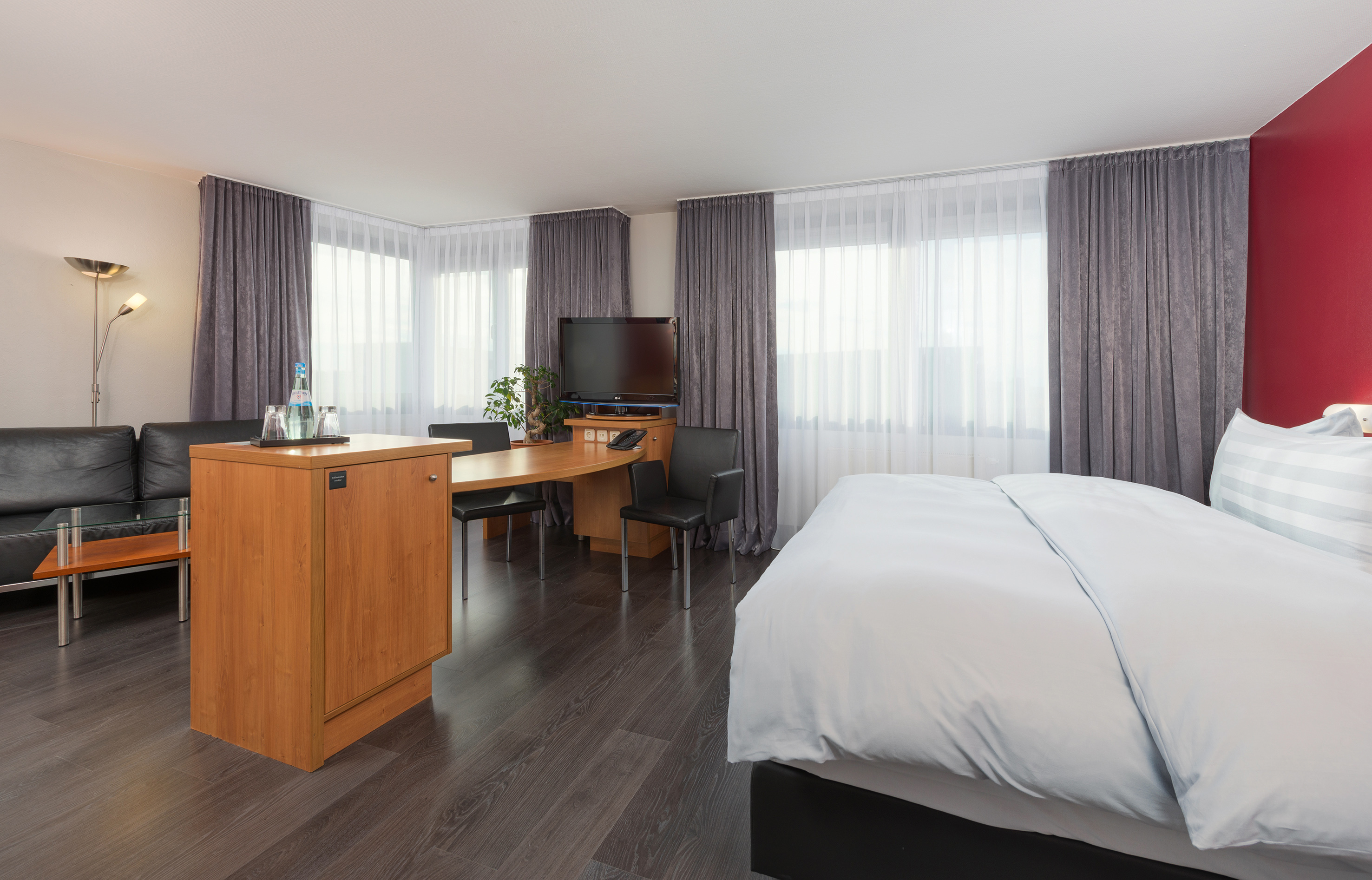 Modern hotel suite featuring a bed, sofa, work desk, and TV.