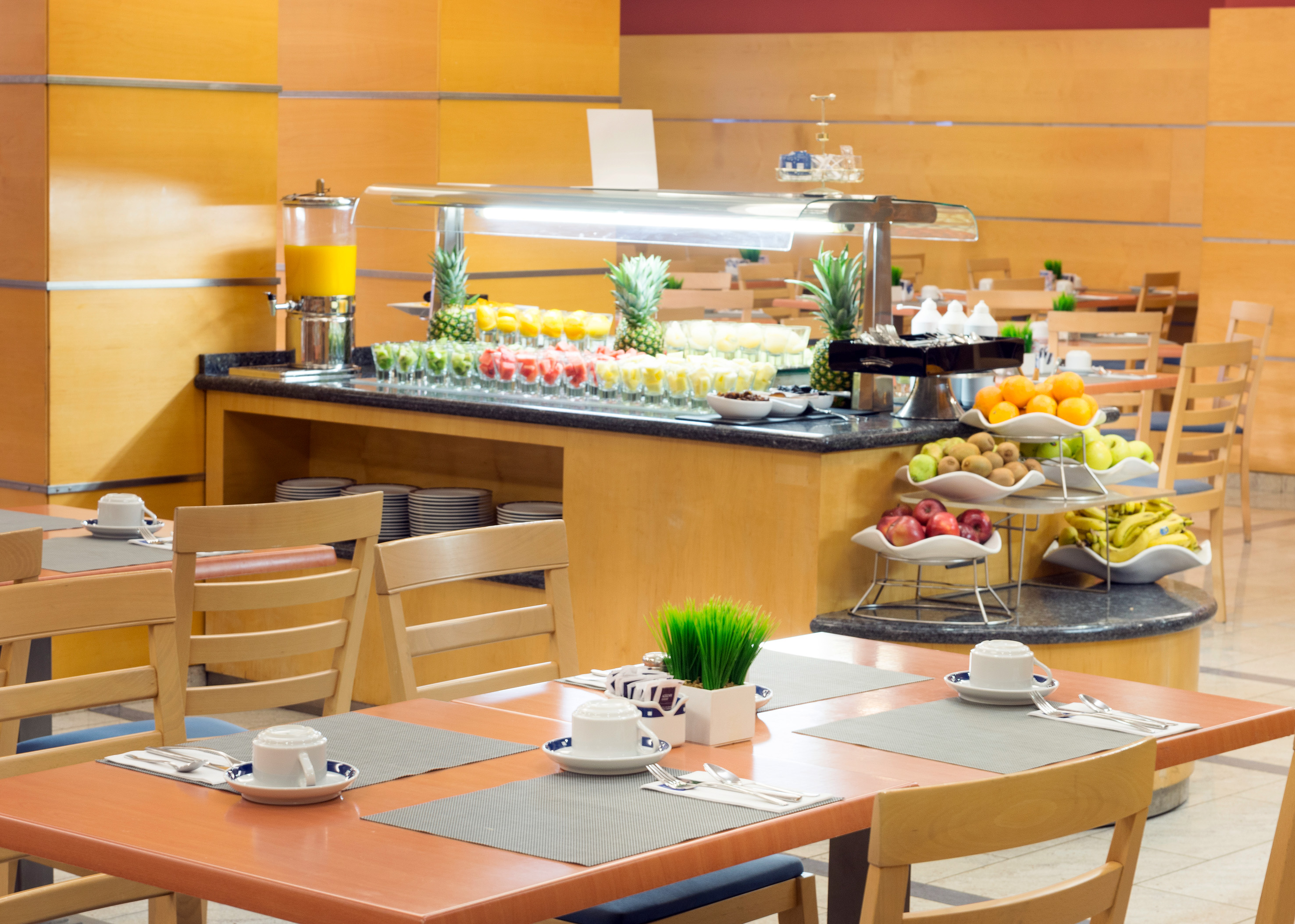 Fresh fruit breakfast buffet in a hotel dining room with set tables.