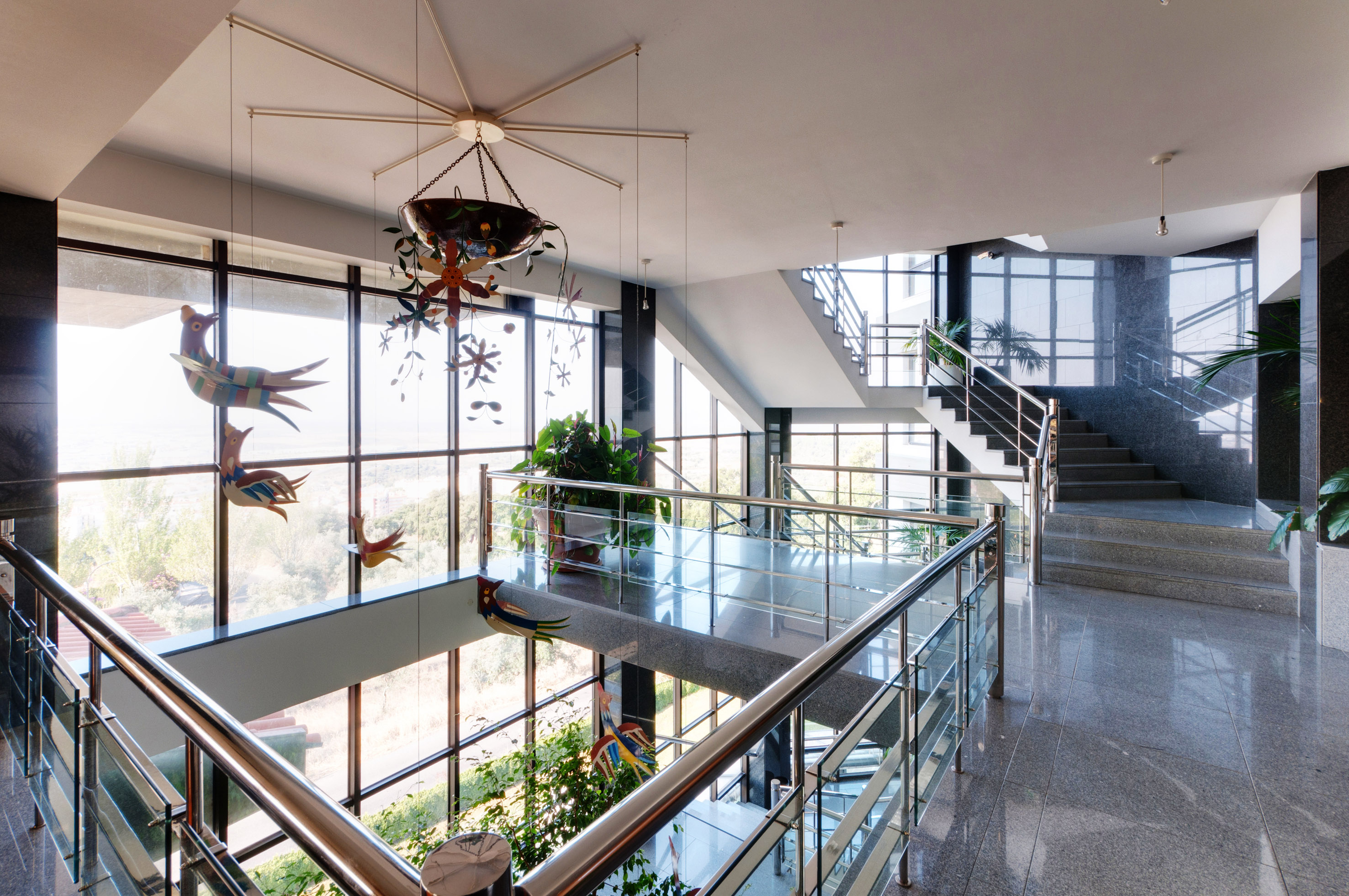 Modern lobby with grand staircase, glass railings, granite floors, and windows.