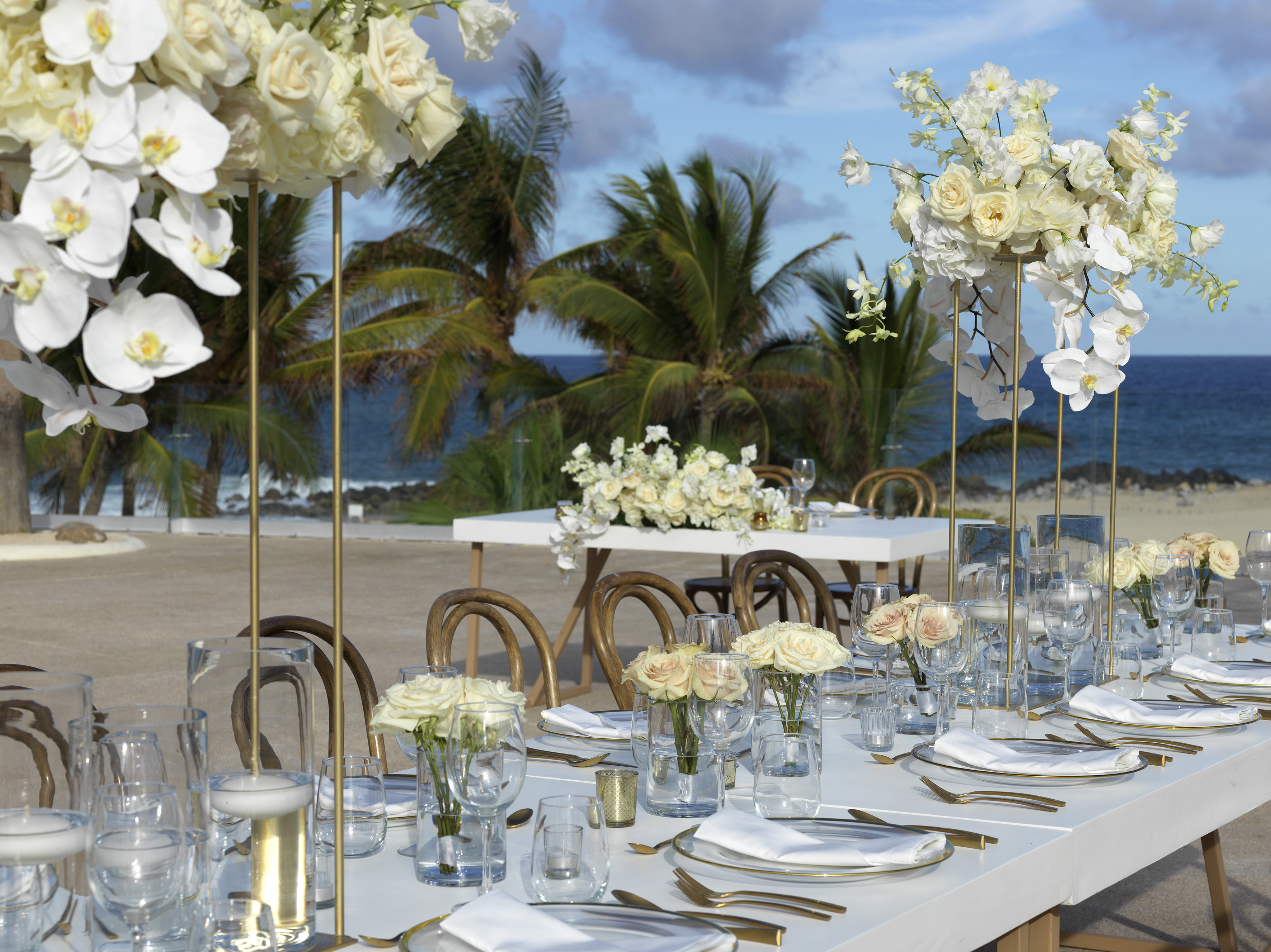 Beach wedding table with white flowers, gold accents, and ocean view.