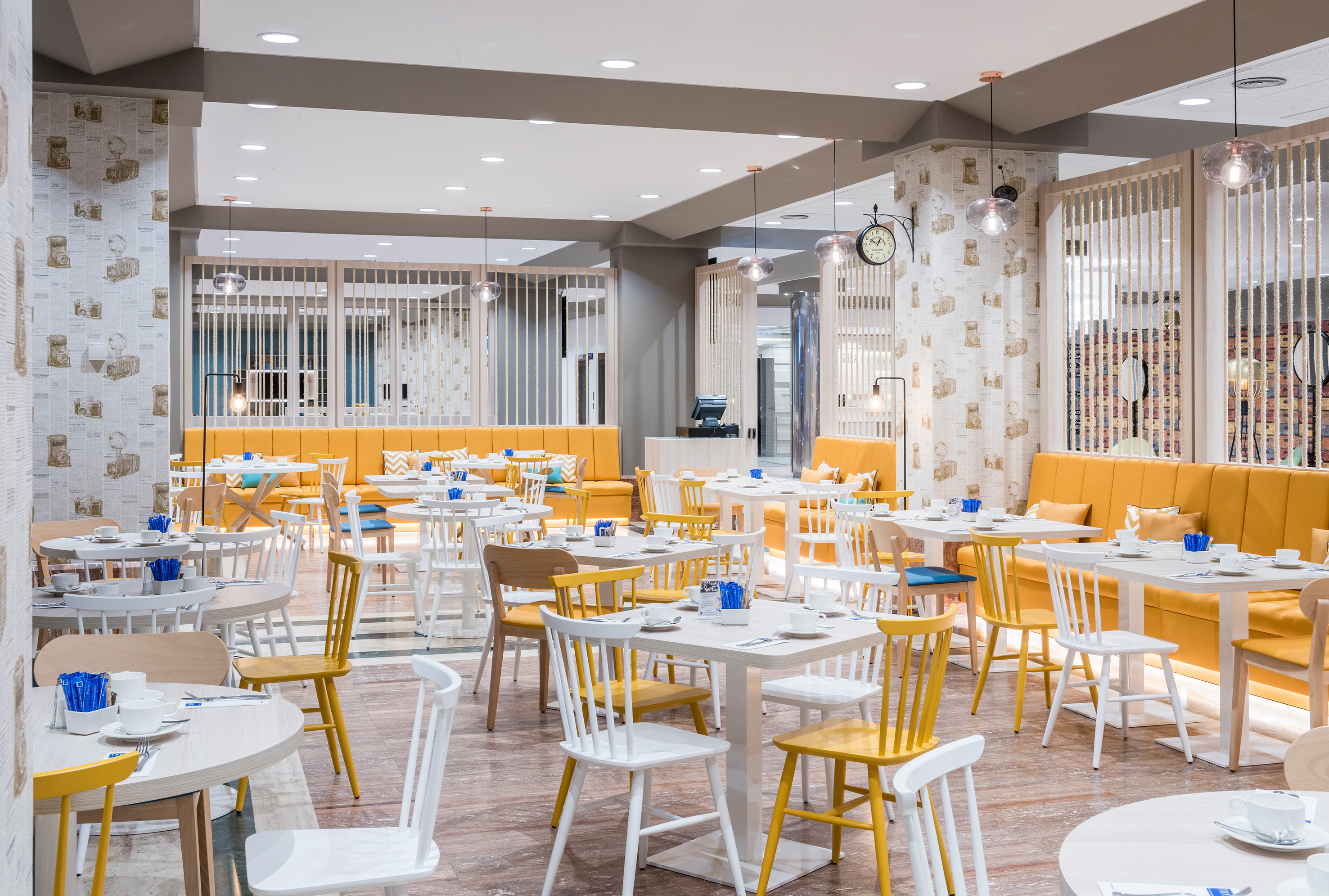 Modern dining room with yellow chairs, orange banquettes, and white tables.