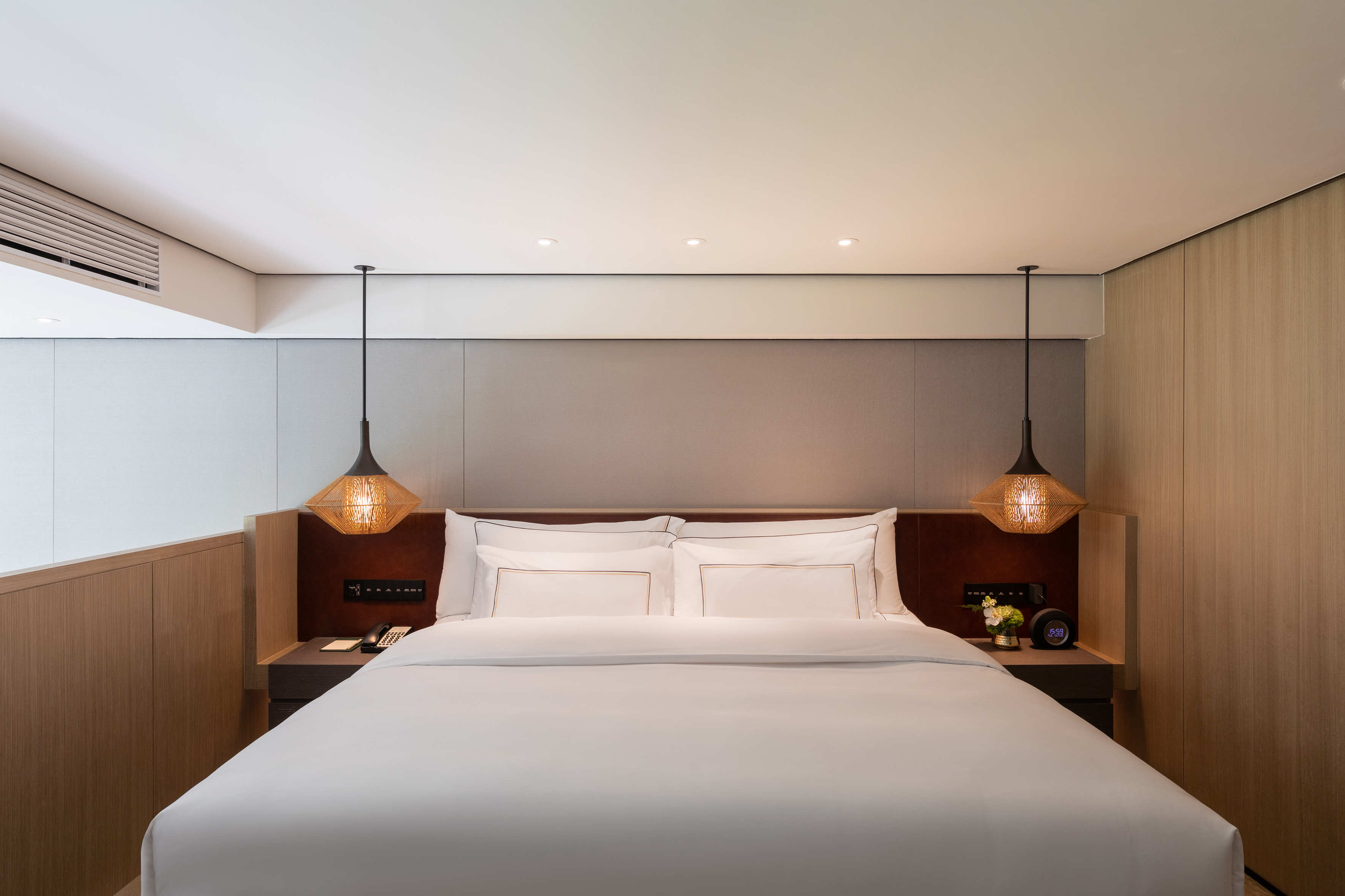 Modern hotel bedroom with king bed, wooden accents, and woven pendant lights.