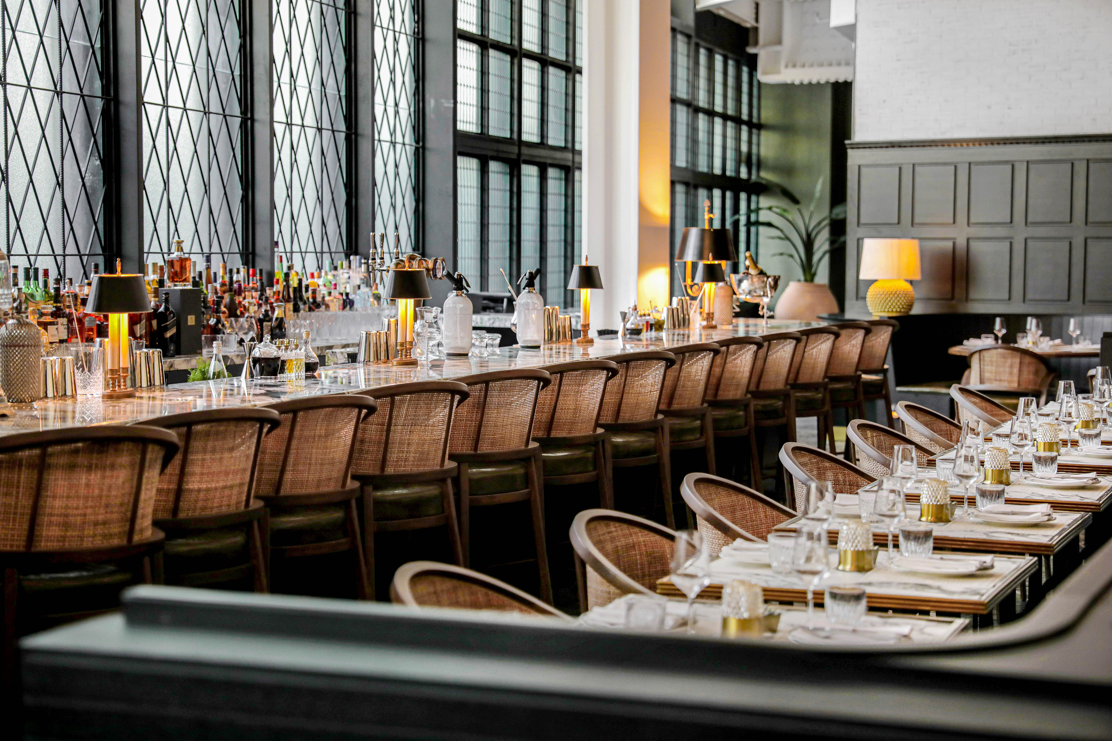 Modern bar and dining room with long counter, stools, and set tables.