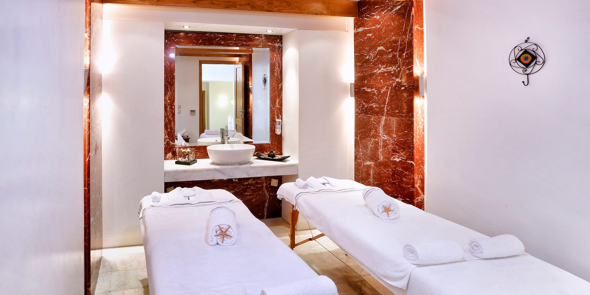 Luxurious spa treatment room with two massage tables and red marble details.