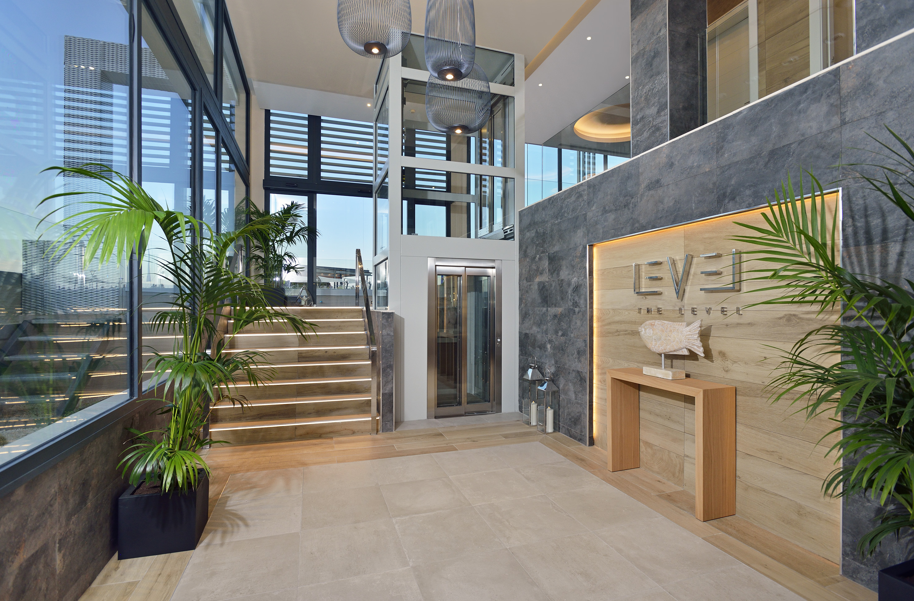 Modern hotel lobby featuring glass elevator, light-up stairs, and stone walls.
