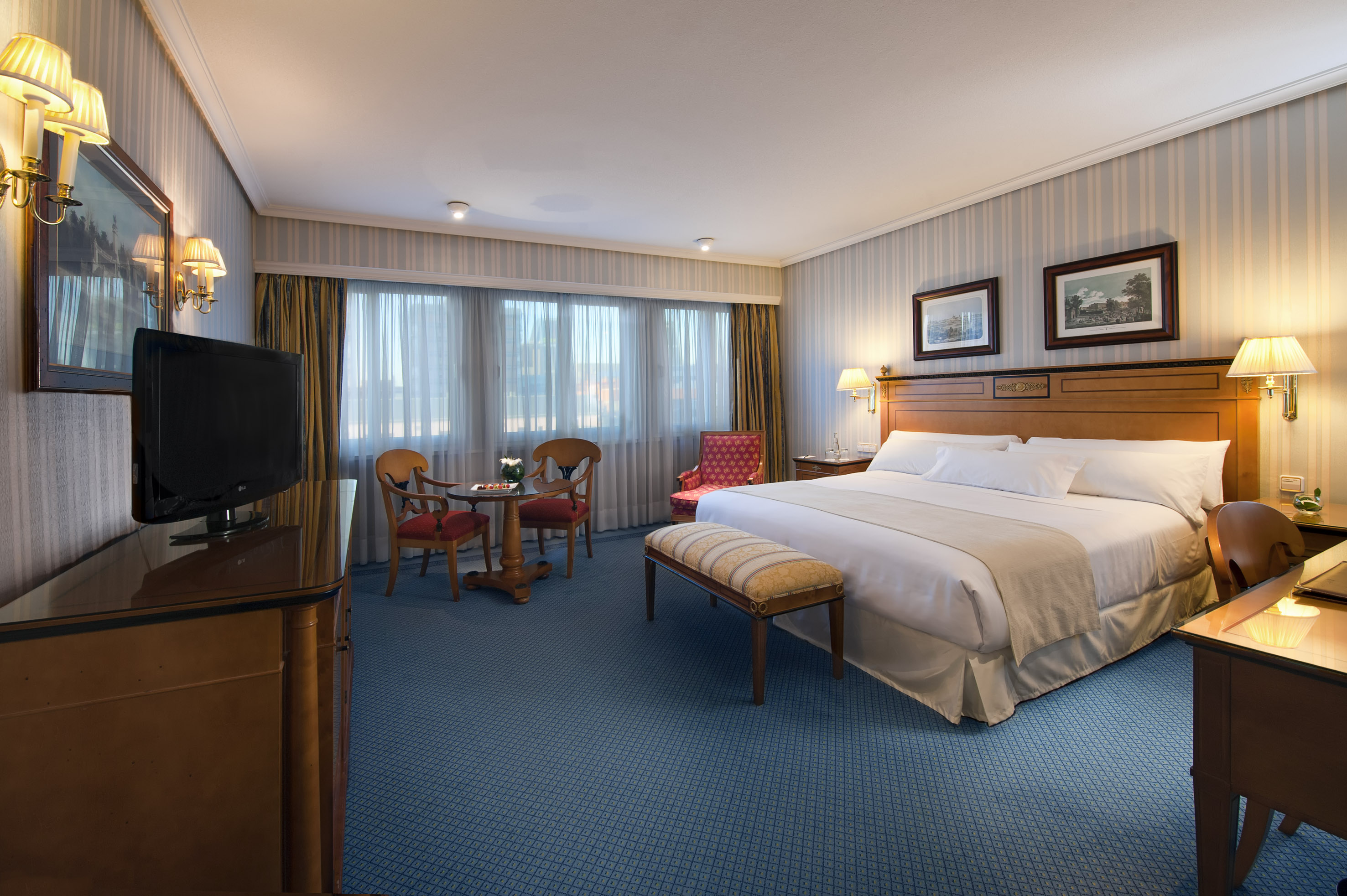 Comfortable hotel guest room with king bed, blue carpet, desk, and seating.