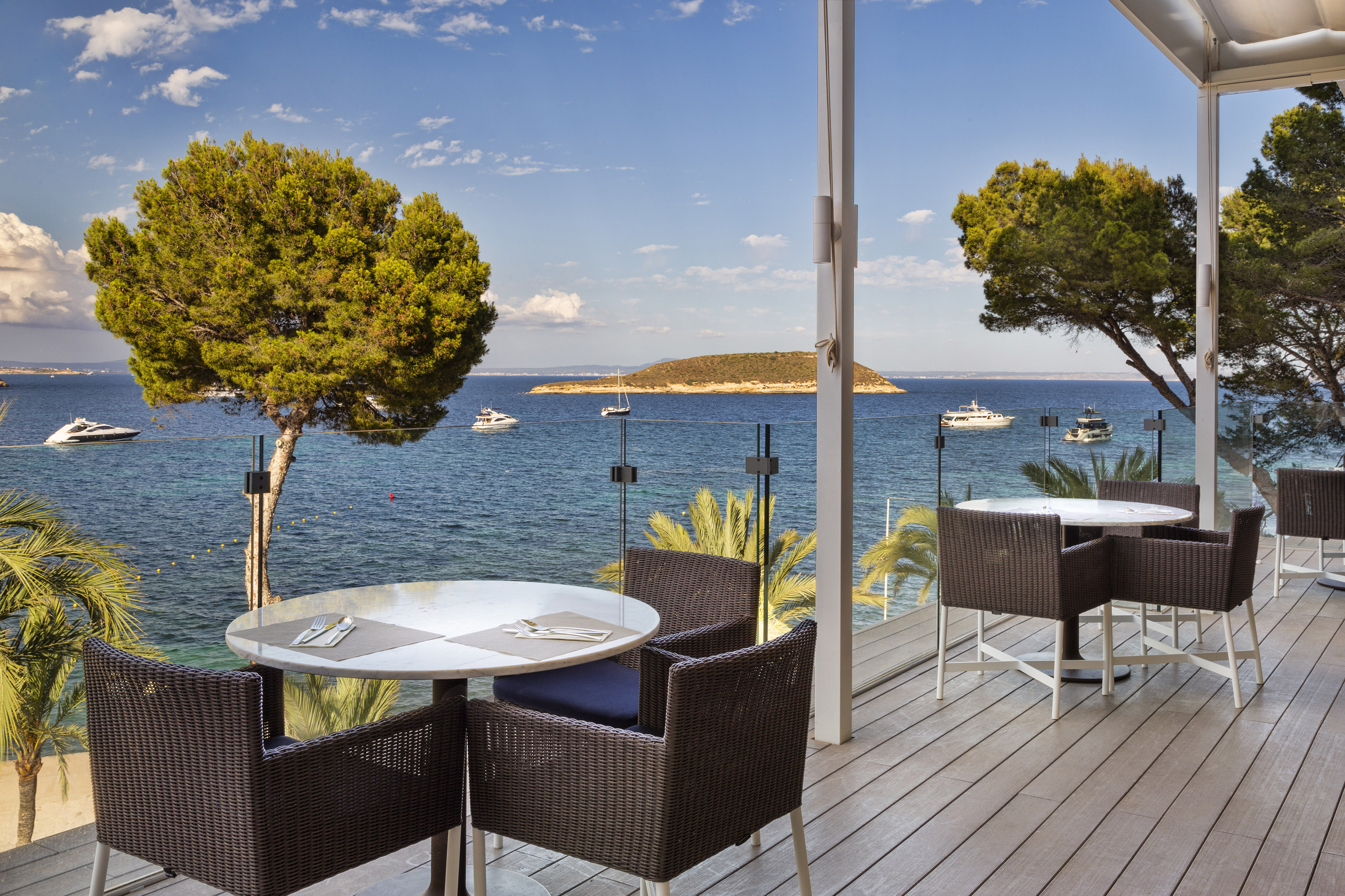 Outdoor dining terrace with sea view, yachts, and distant island.