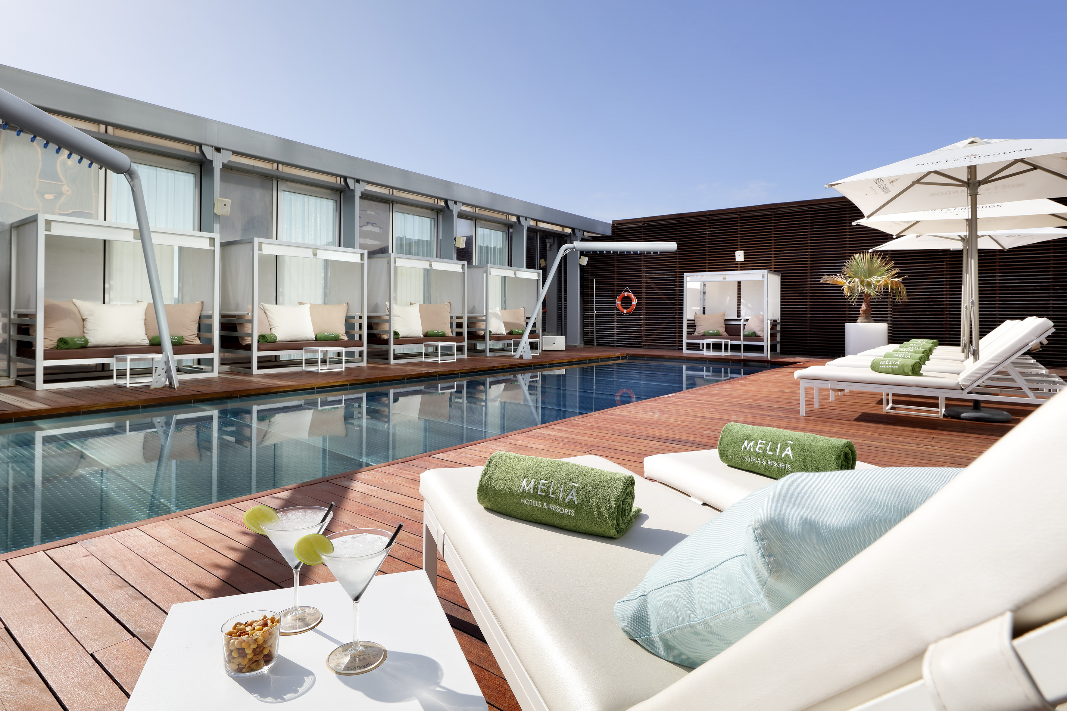Meliá rooftop pool with lounge chairs, daybeds, and cocktails on a wooden deck.