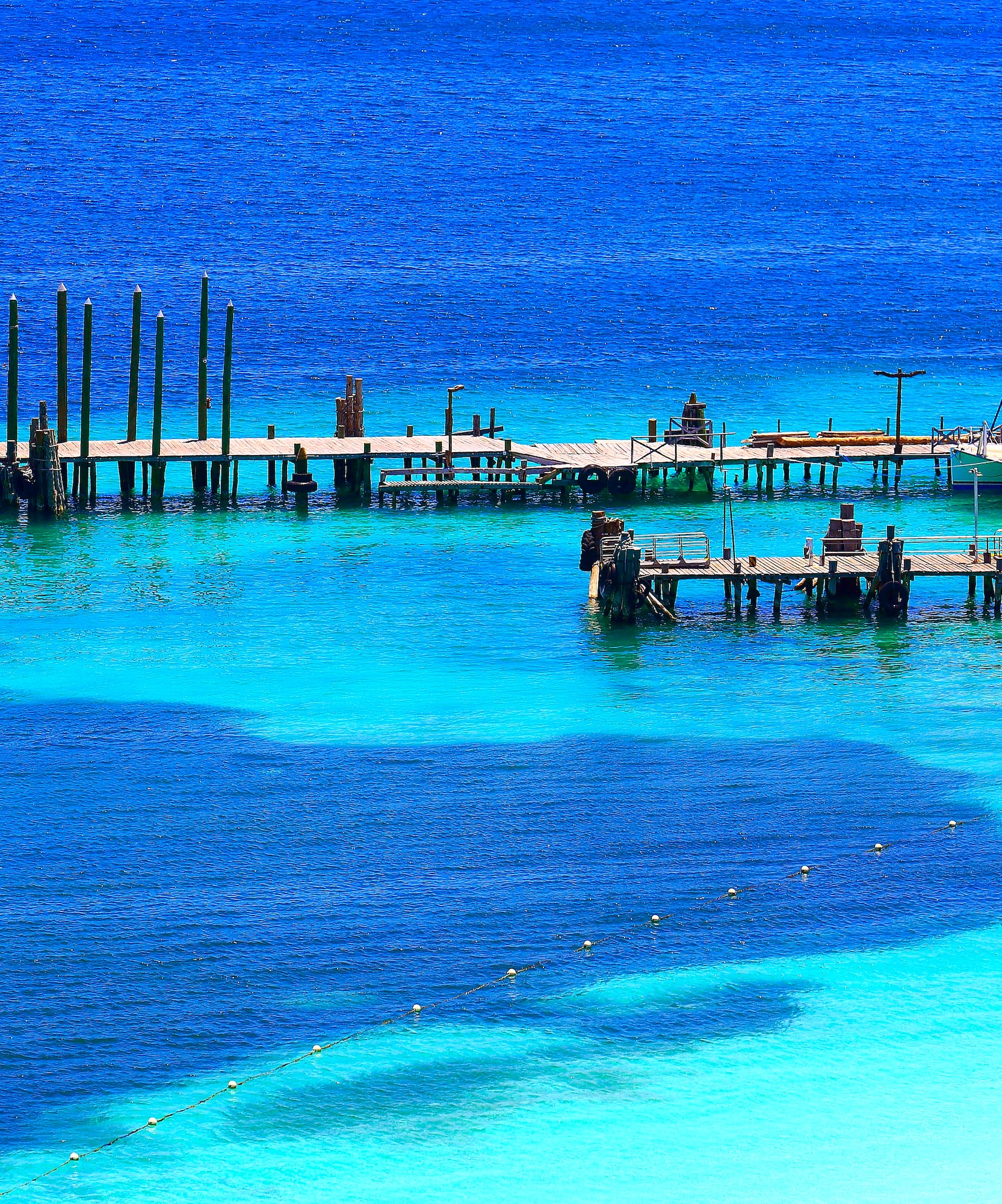 Stunning blue and turquoise ocean with wooden piers and a white catamaran.