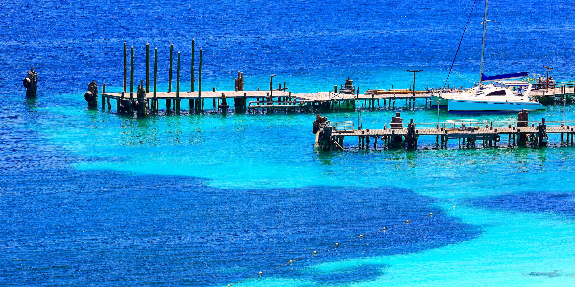 Muelles de madera y velero en aguas cristalinas azul turquesa.
