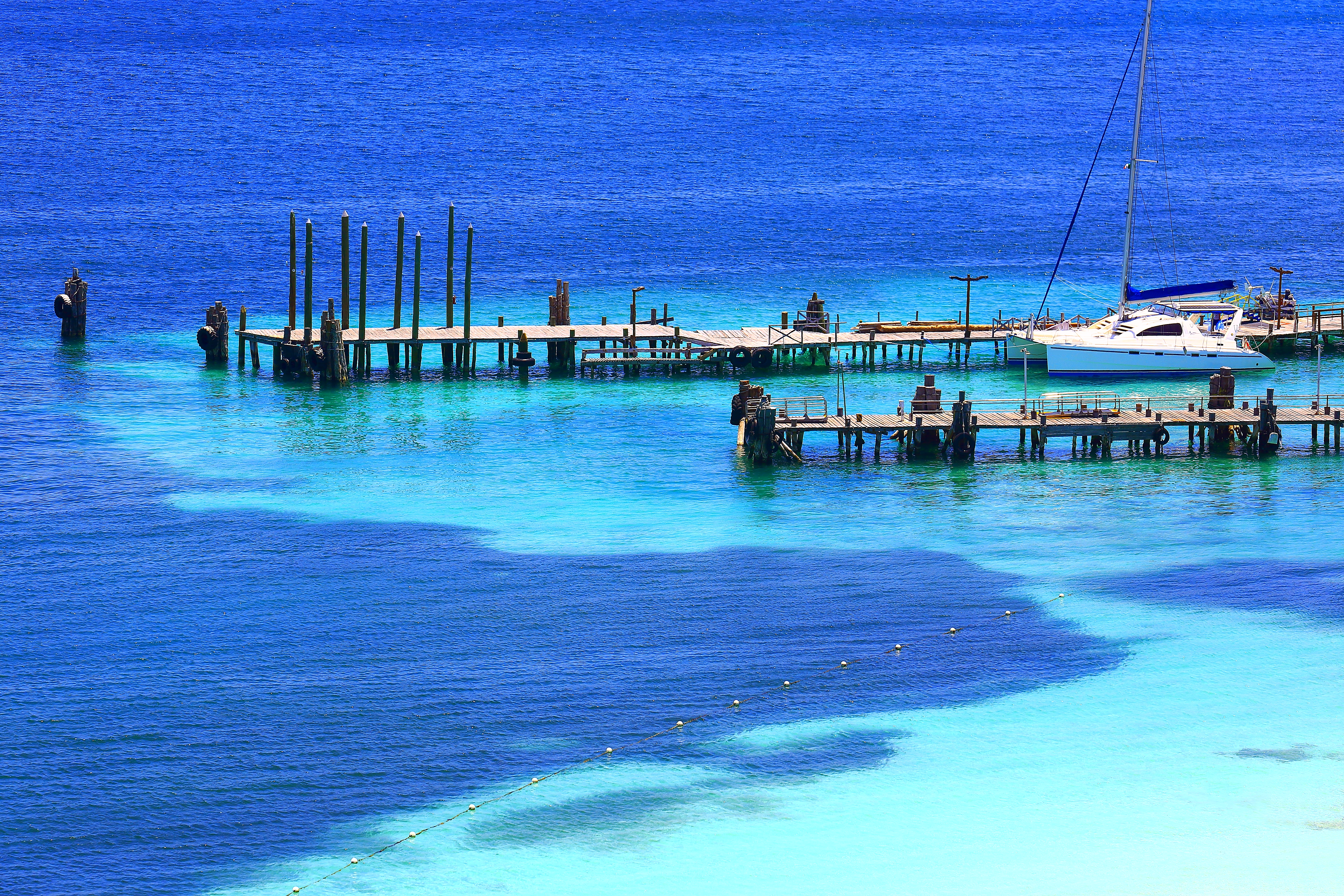 Stunning blue and turquoise ocean with wooden piers and a white catamaran.