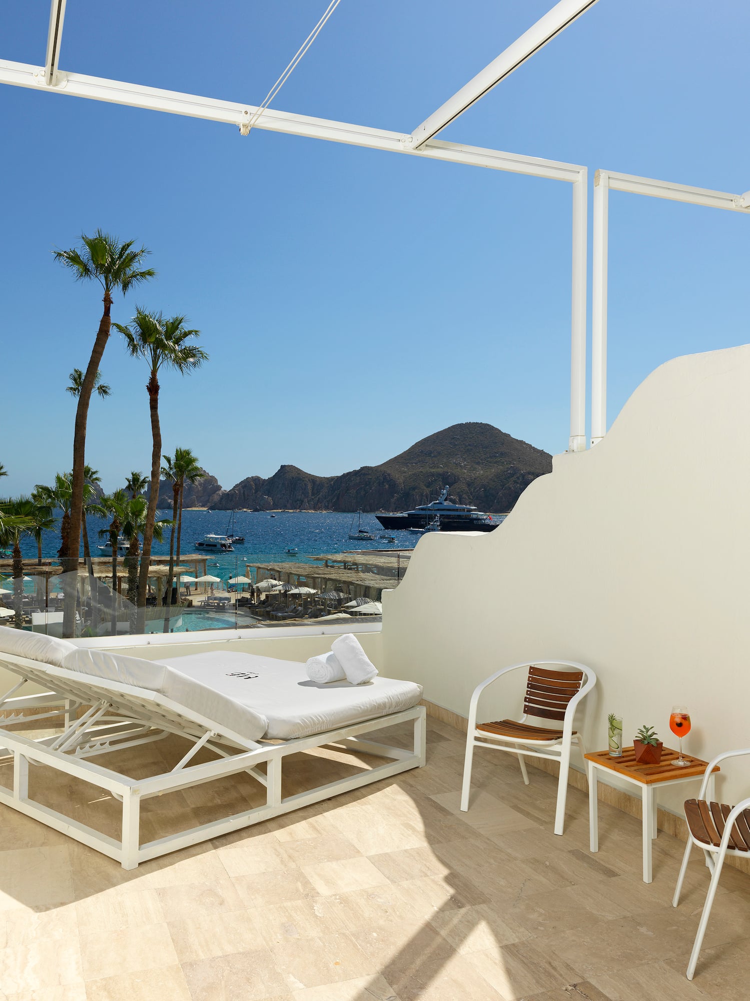 Tropical ocean view balcony with lounge chair, palm trees, and outdoor seating.