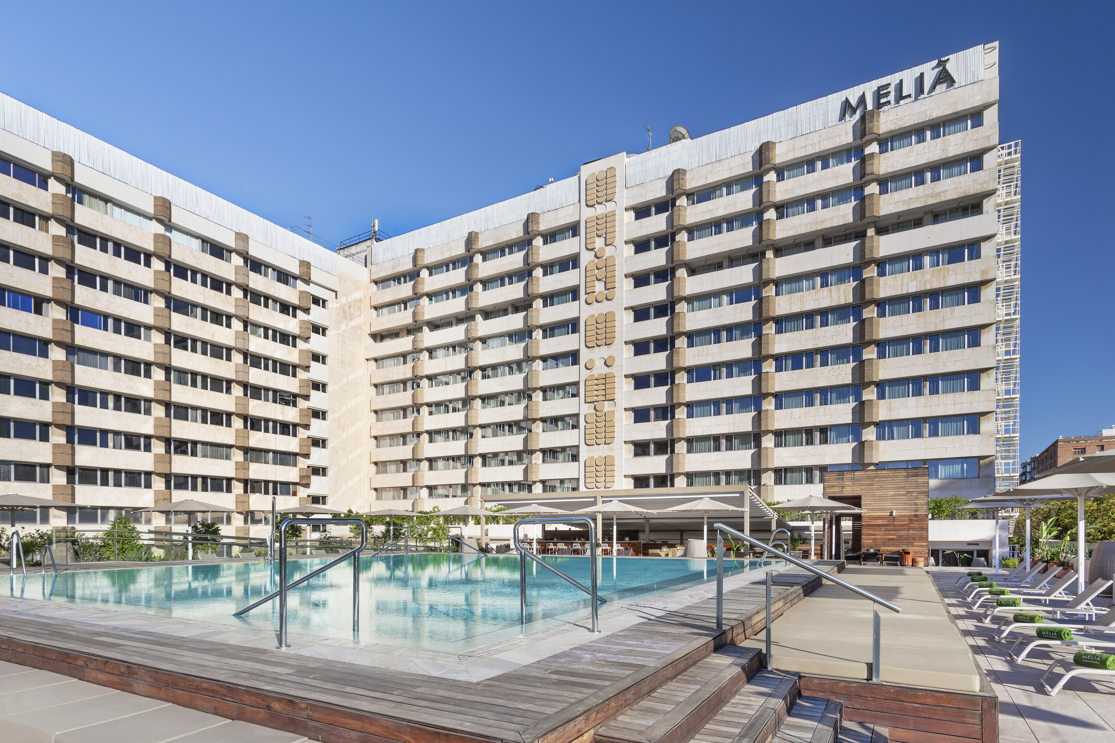Melia Hotel building exterior with large outdoor swimming pool and sun loungers.