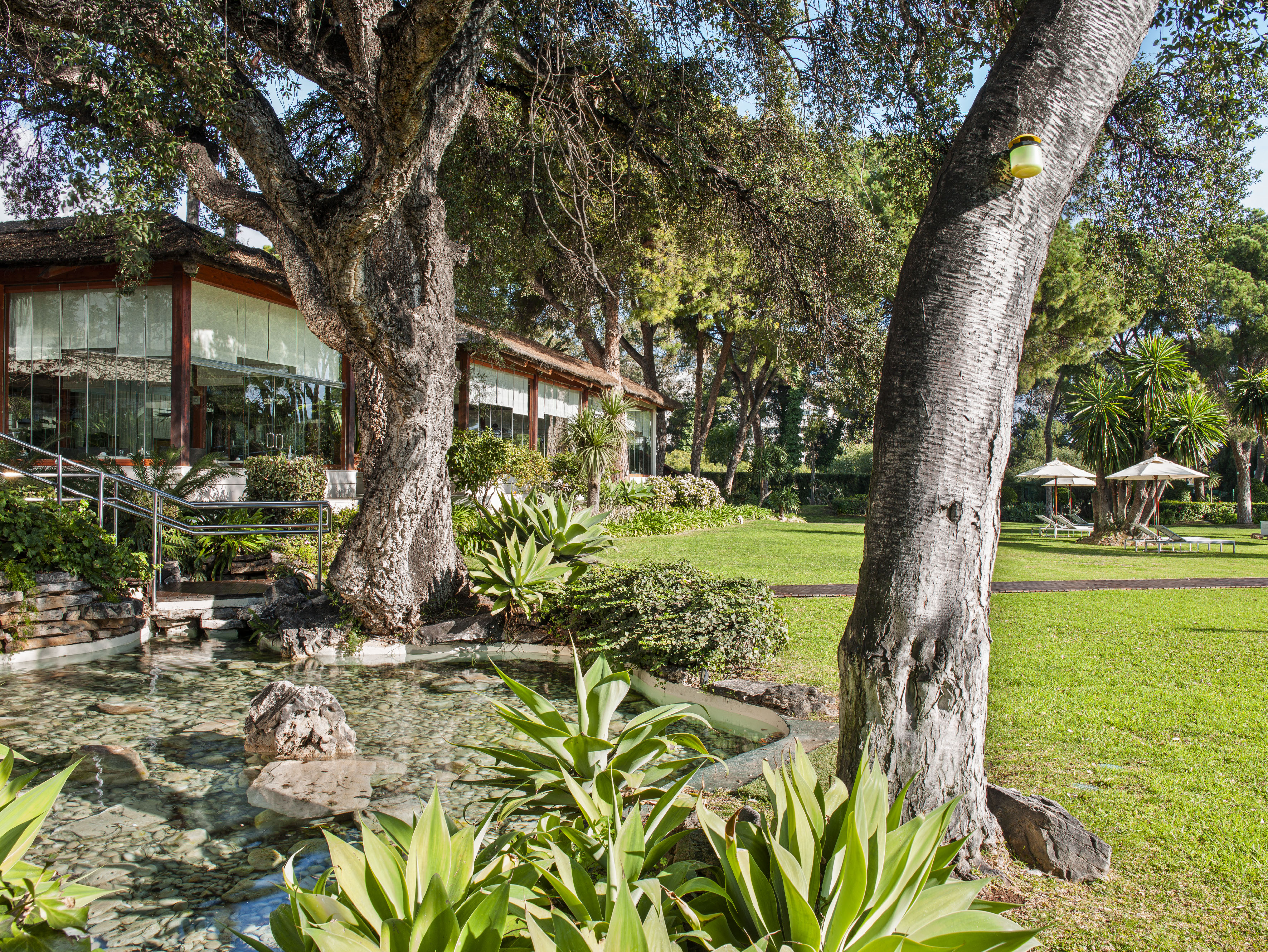 Green garden landscape with pond, large trees, and a resort building.