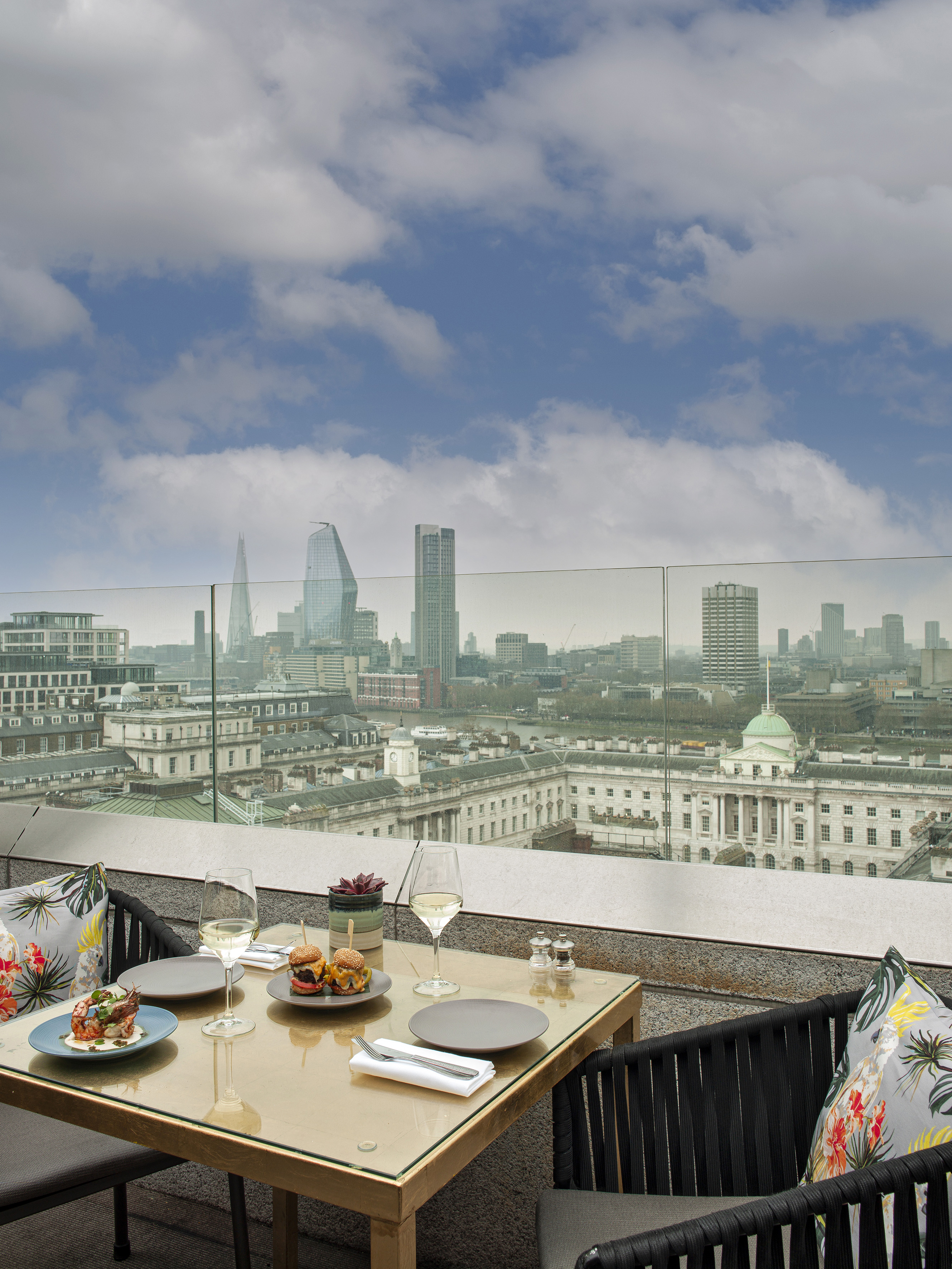 Rooftop dining table with food, wine, and panoramic London skyline view.