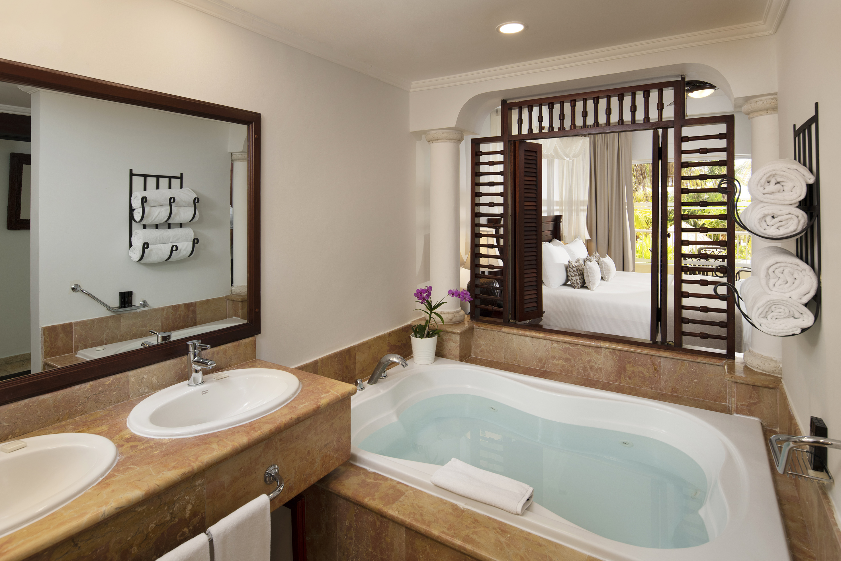 Hotel bathroom with soaking tub, dual sinks, and open view to adjoining bedroom.
