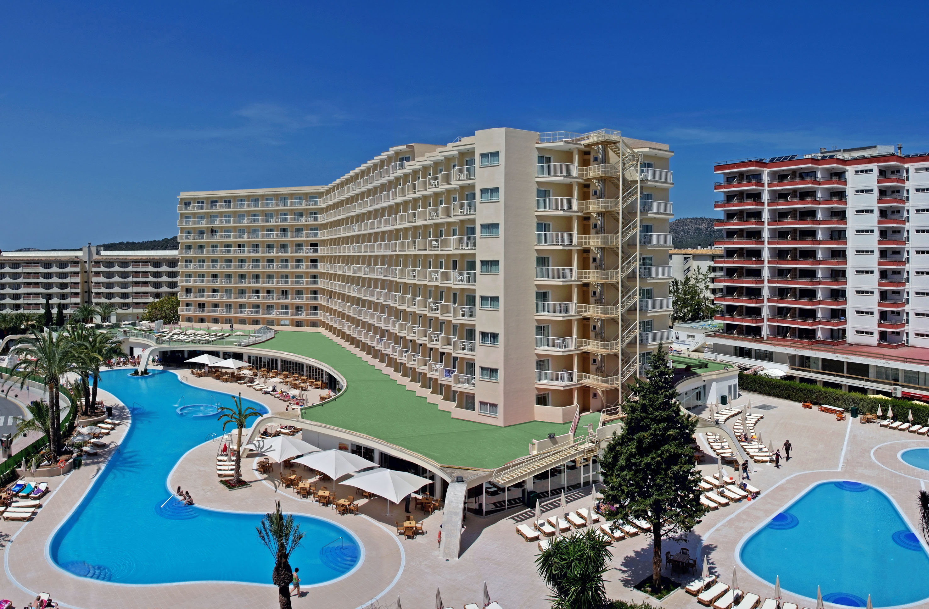 Sunny resort hotel with large swimming pool and terraced balconies.