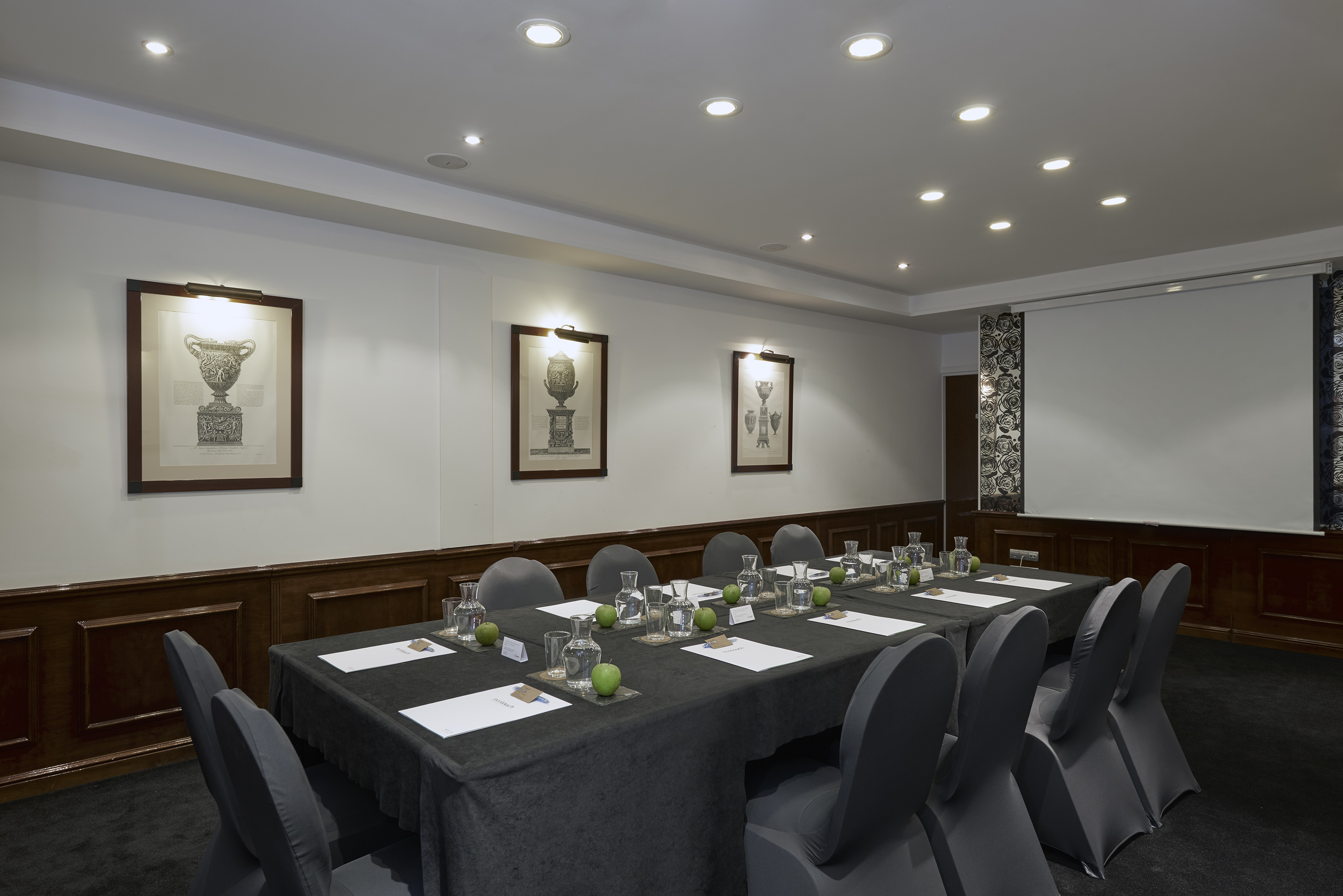 Professional meeting room with long table, grey chairs, and presentation screen.