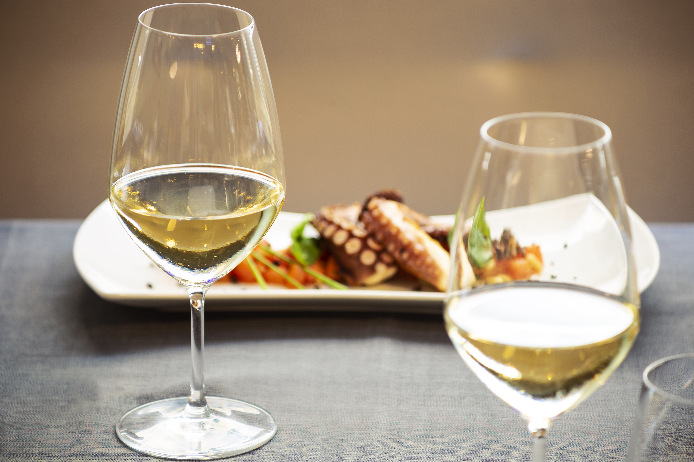 White wine glasses and grilled octopus seafood dish on a table. - Meliá Genova, Genoa