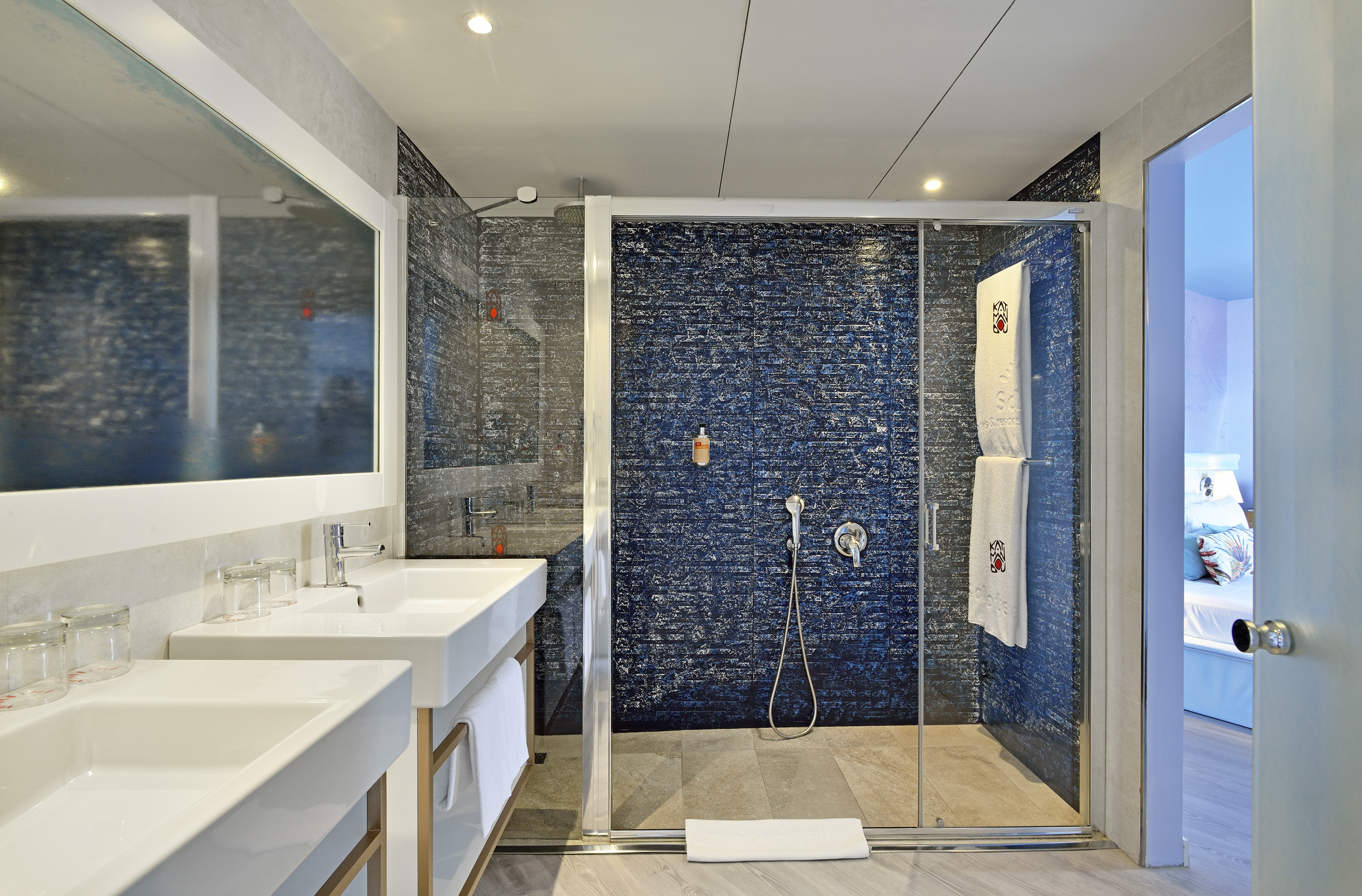 Modern bathroom with dual sinks, glass walk-in shower, and blue textured tiles.