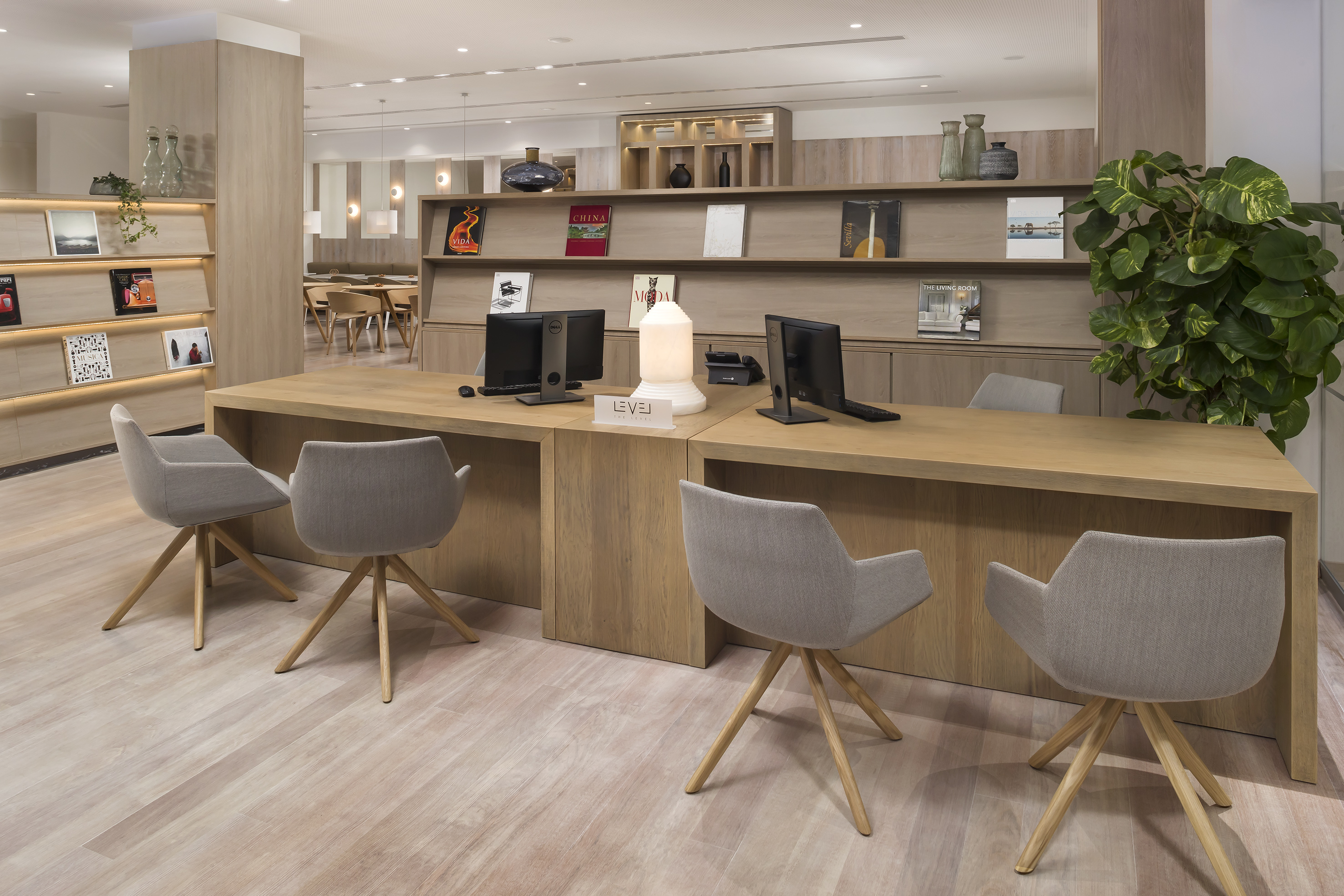 Modern hotel business center with light wood desks, computers, and gray chairs.