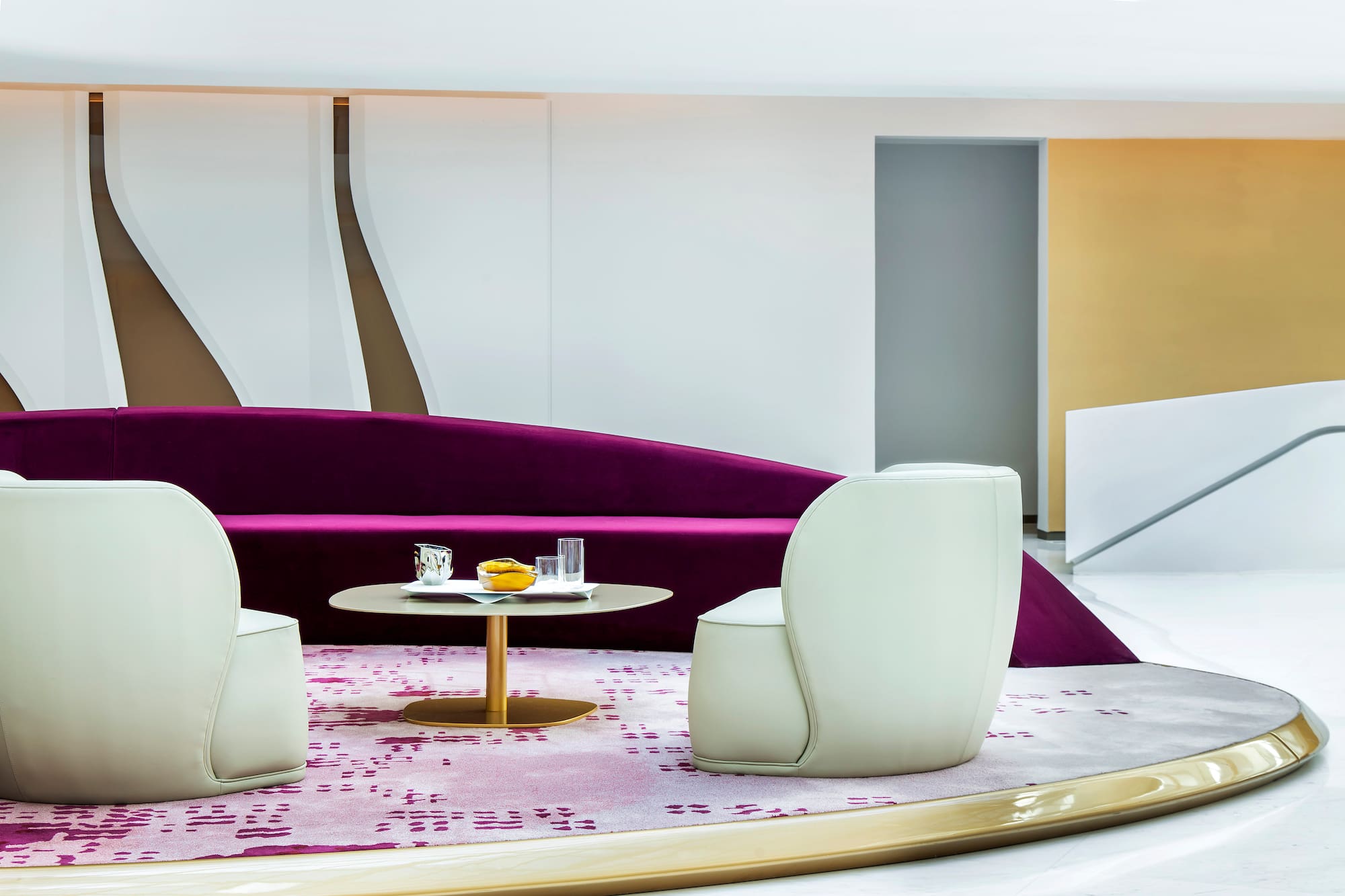 Modern lounge with curved purple sofa, beige armchairs, gold details.