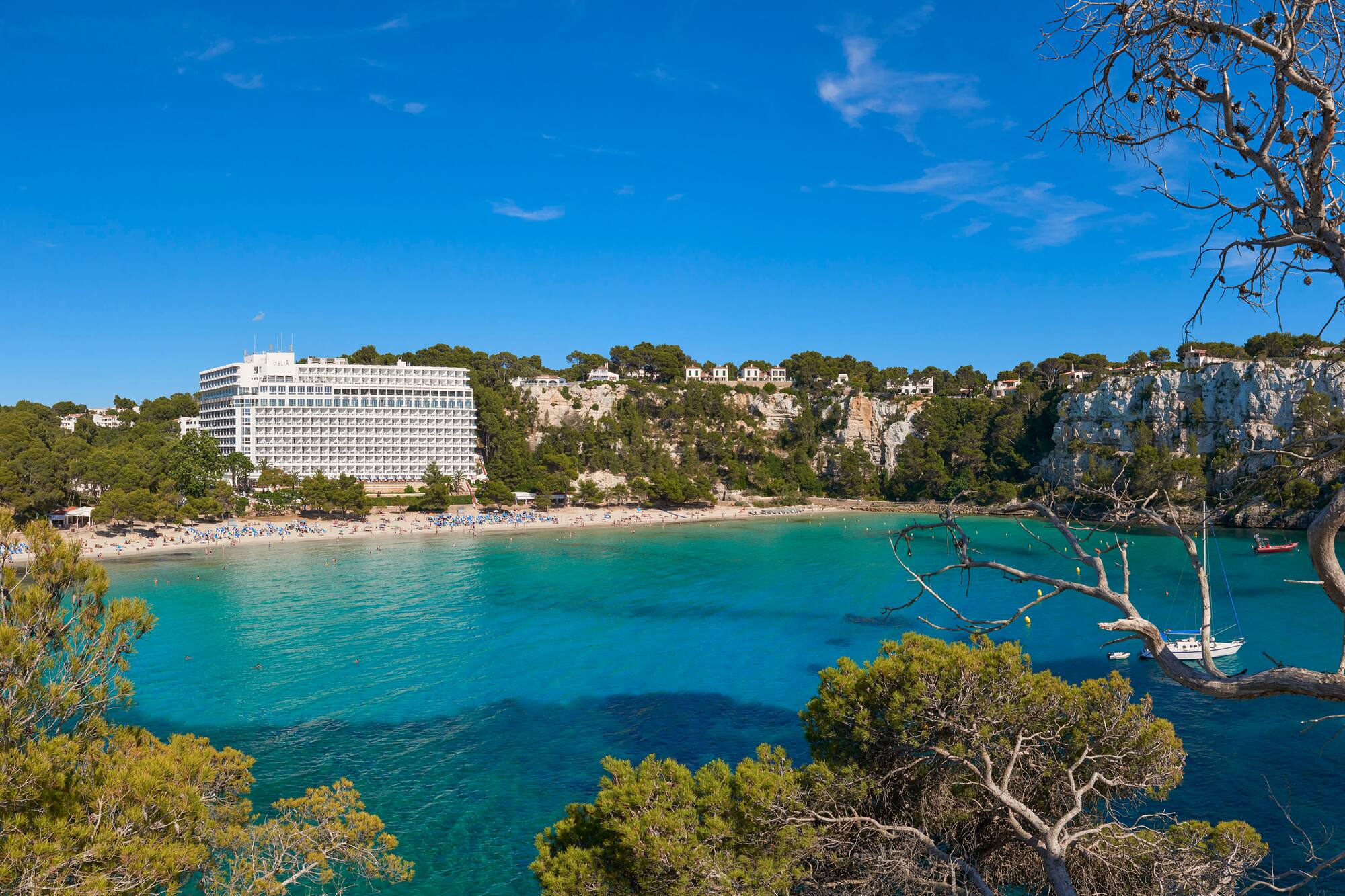 Cala Galdana beach Menorca, turquoise sea, resort hotel, and green cliffs.