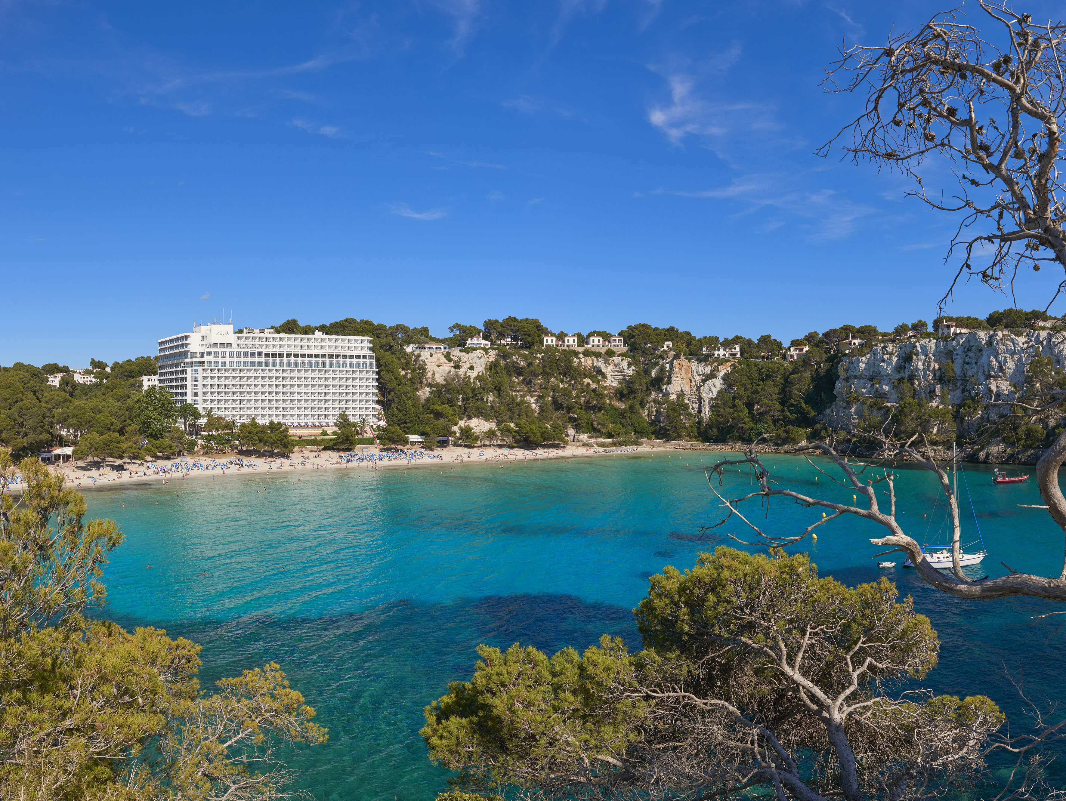 Cala Galdana beach Menorca, turquoise sea, resort hotel, and green cliffs.