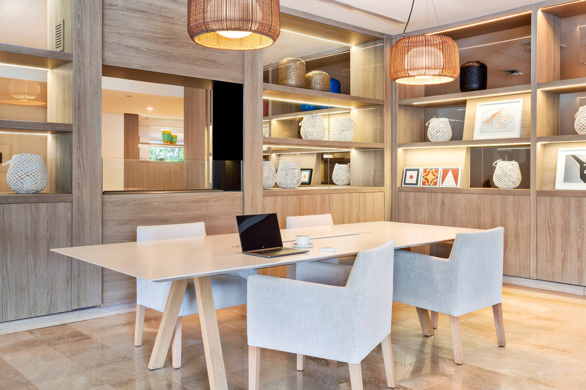 Modern meeting room with white table, grey chairs, laptop, and wooden shelving.