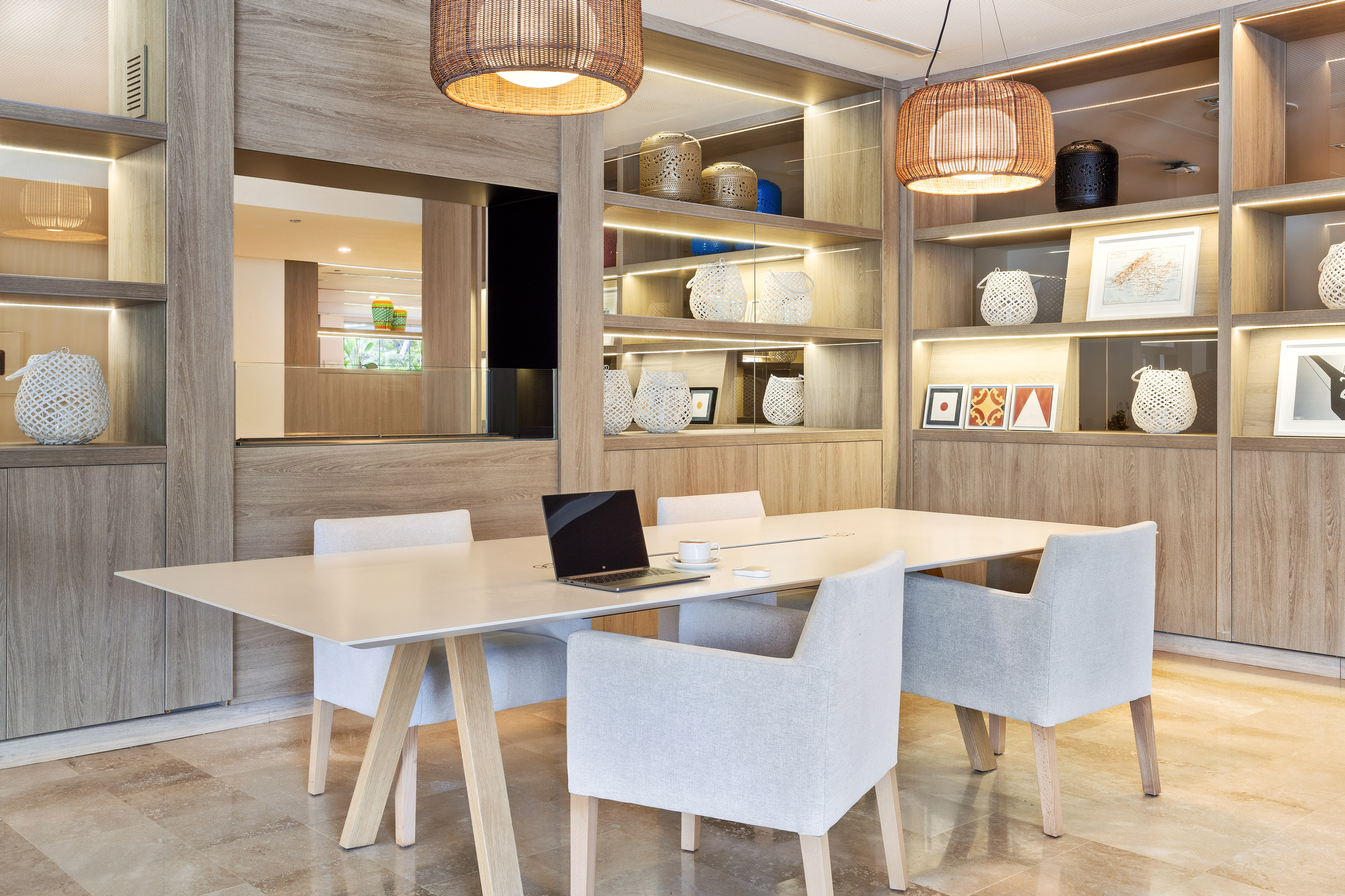 Modern meeting room with white table, grey chairs, laptop, and wooden shelving.