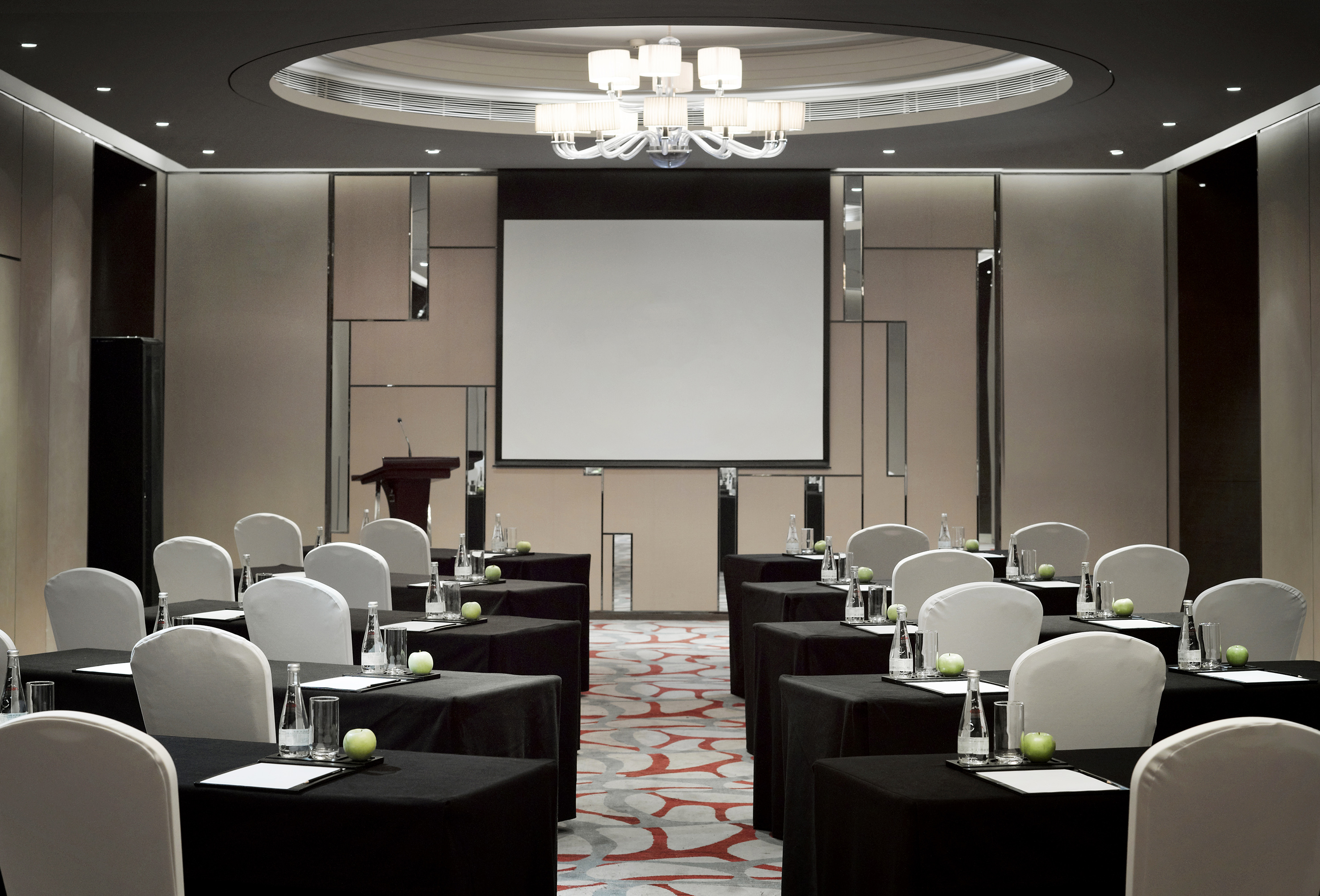 Spacious conference room with projector screen, podium, black tables, white chairs.