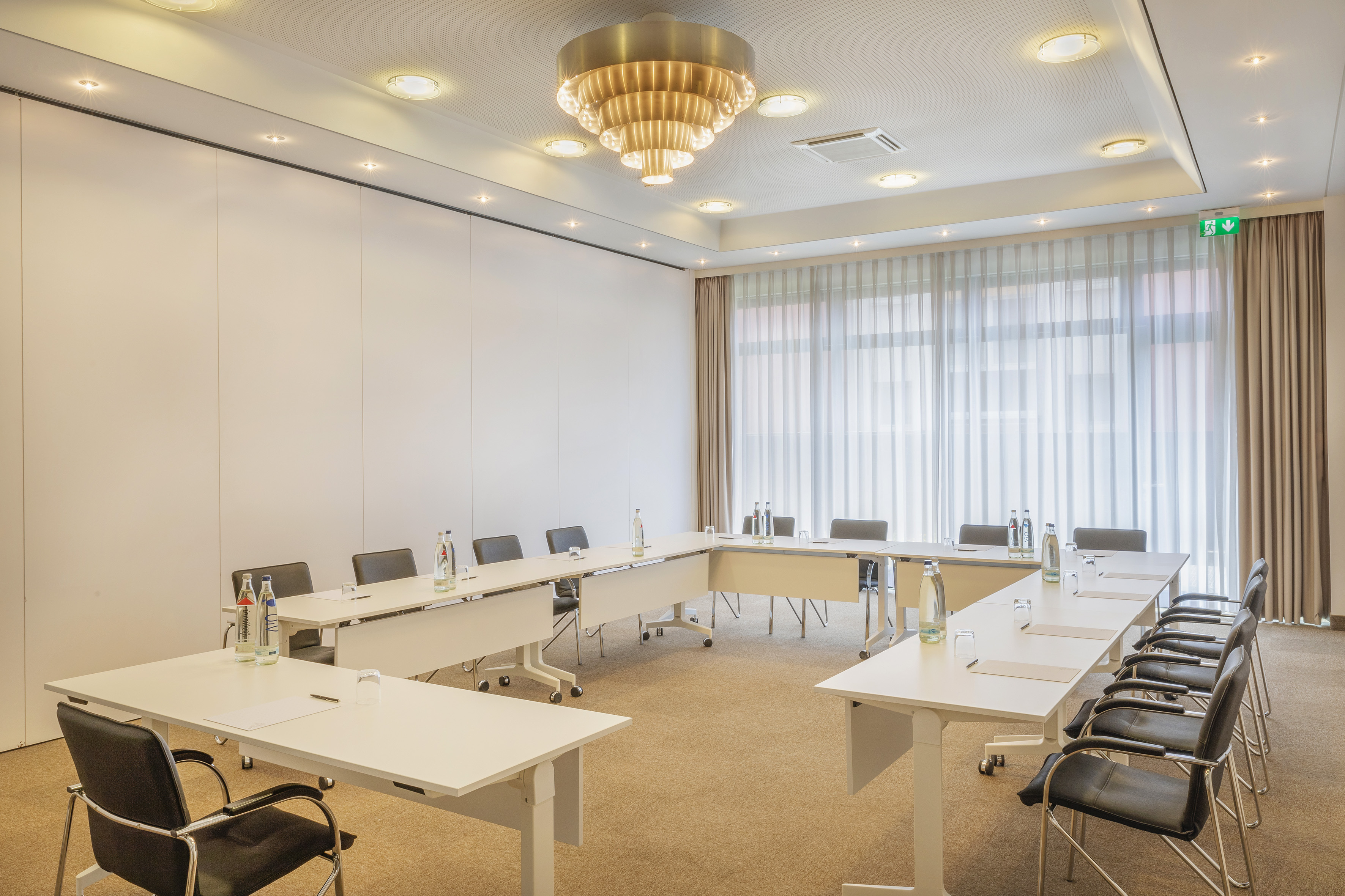 Bright, modern U-shape meeting room with tables, chairs, and chandelier.