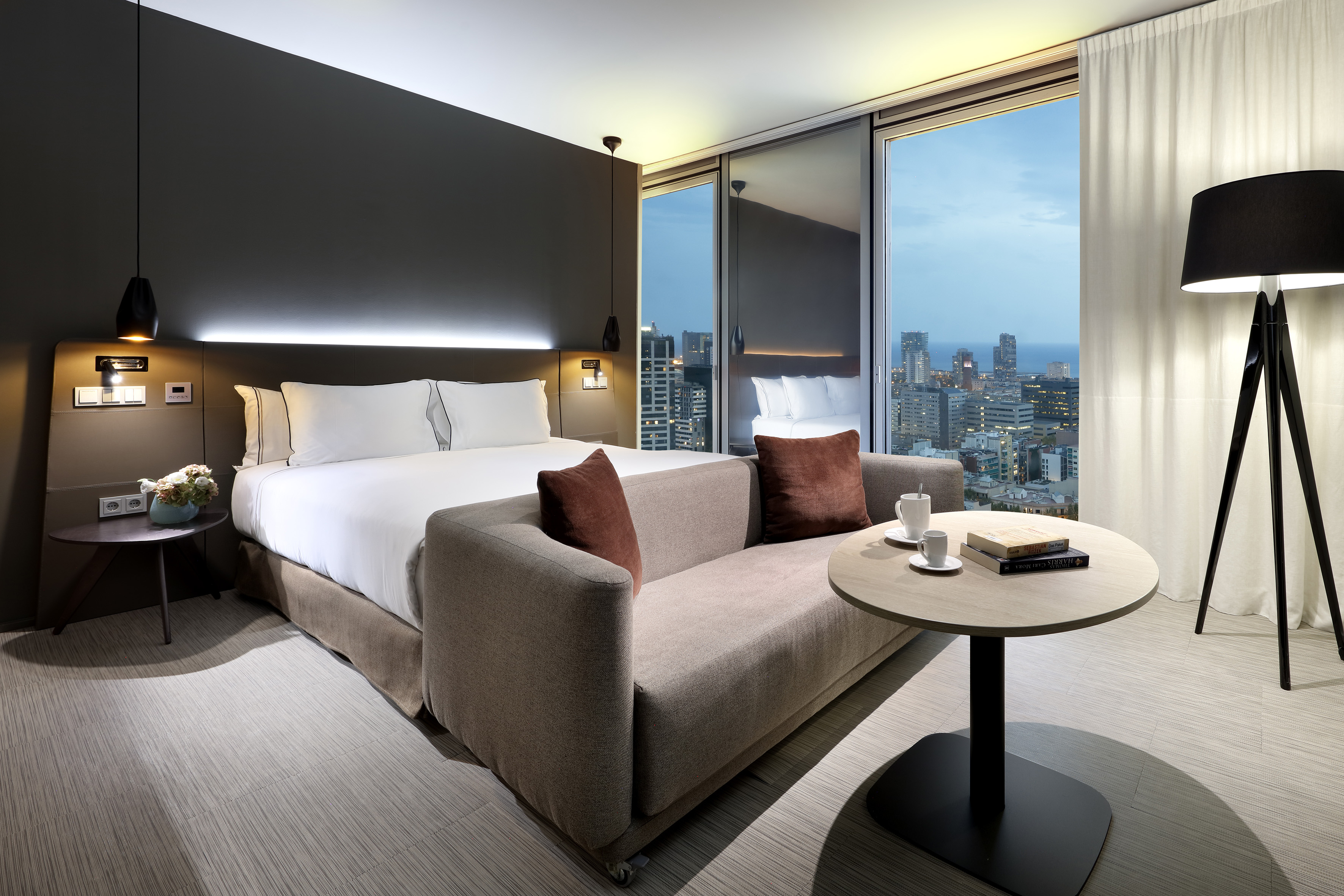 Modern hotel room with king bed, sofa, and city skyline ocean view.