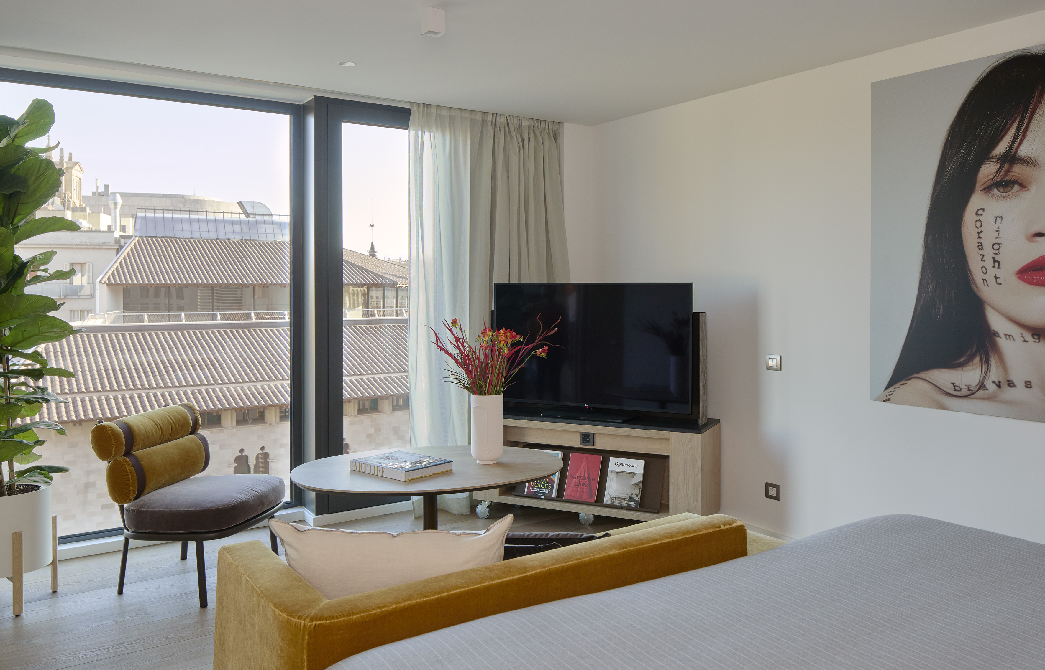 Modern hotel suite with city view, TV, plant, and large contemporary artwork.