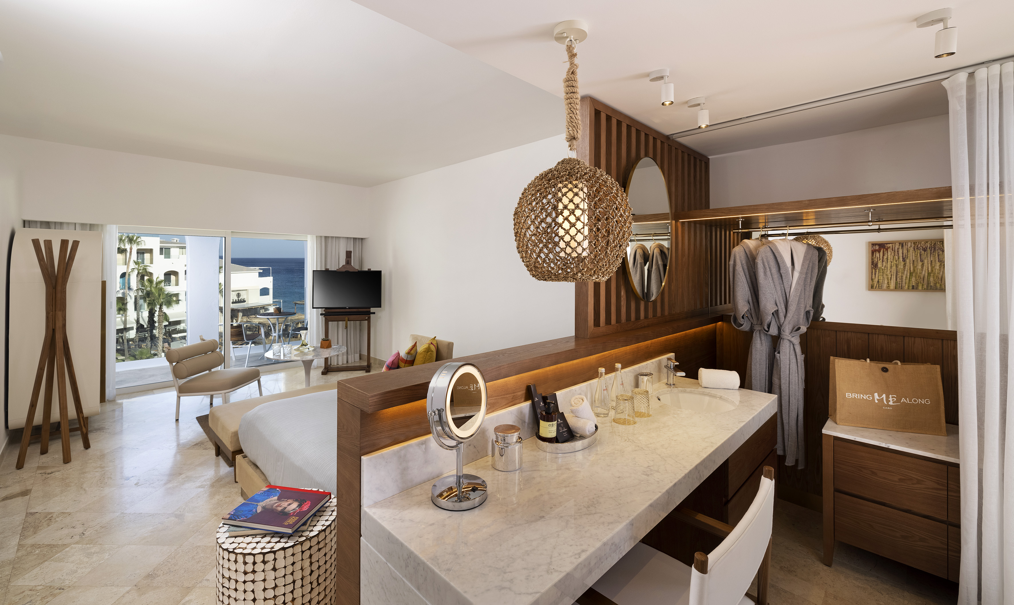 Tropical hotel room with ocean view balcony, vanity, and open wardrobe.